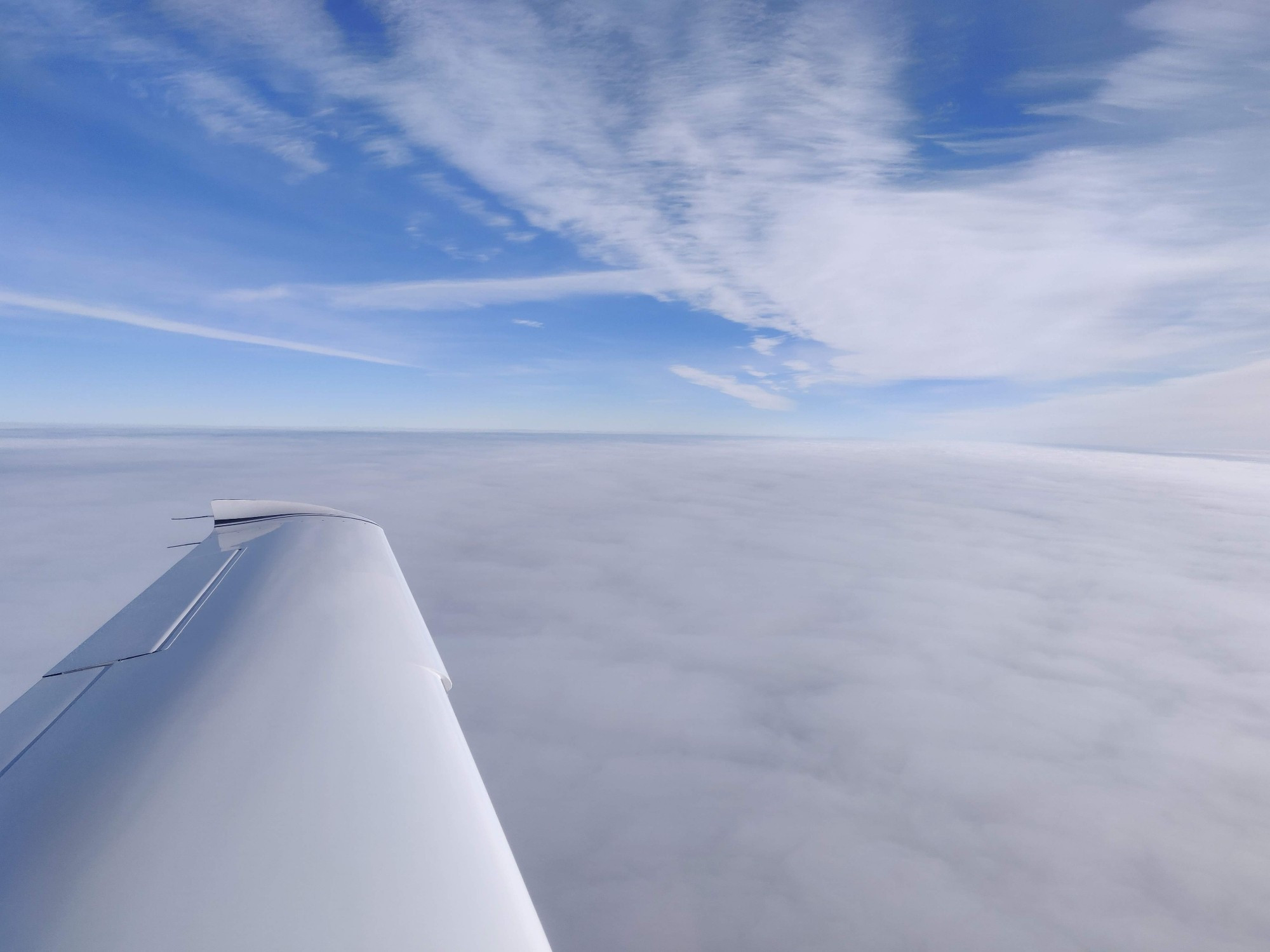 a photo across the white wing of an SR20 airplane of a overcast cloud layer with blue skies above