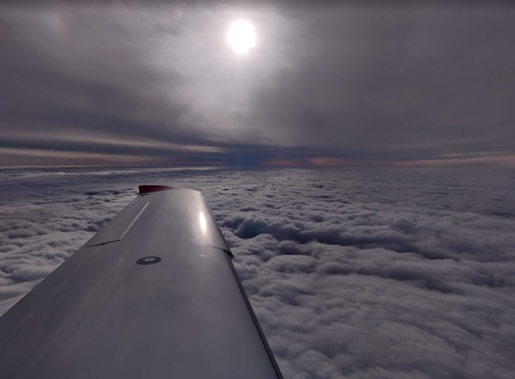 photo over the silver wing of an SR22 airplane flying between two solid layers of clouds