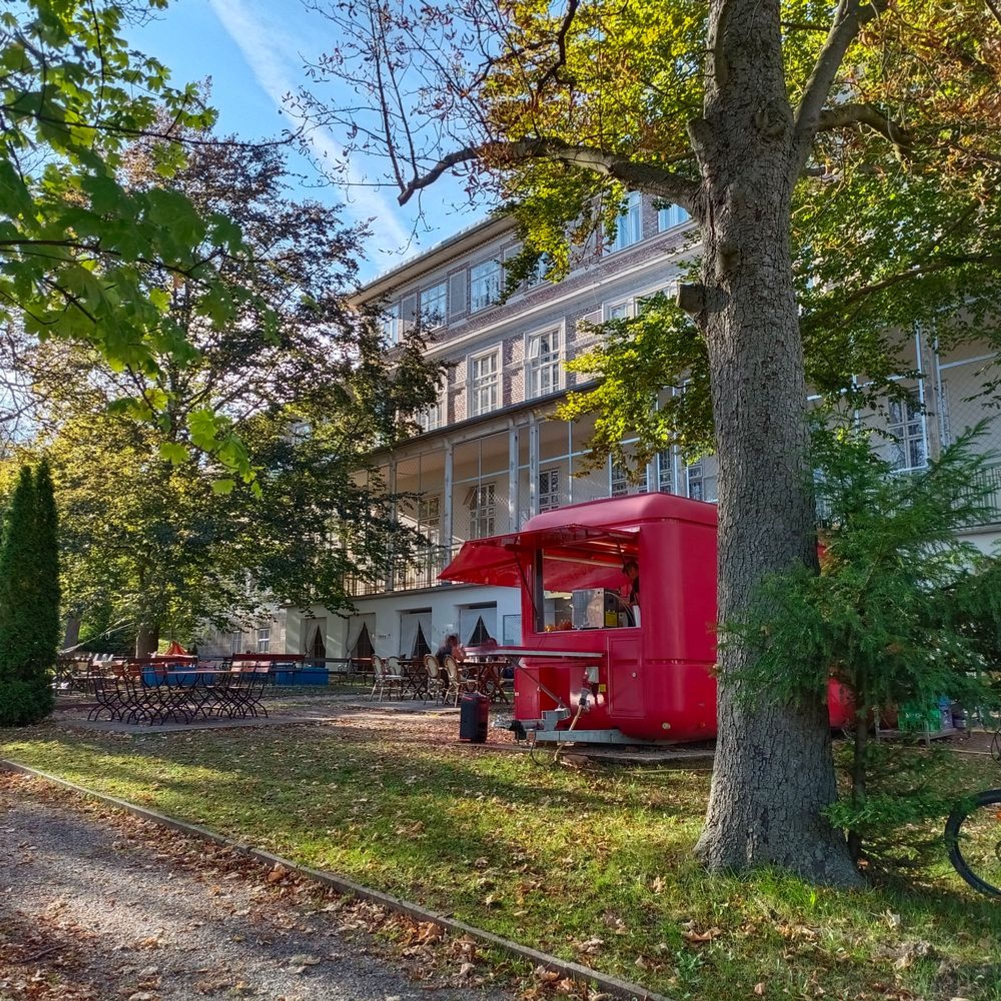 ein roter Foodtruck steht im Park vor einem Spitalspavillon aus dem Jugendstil. 