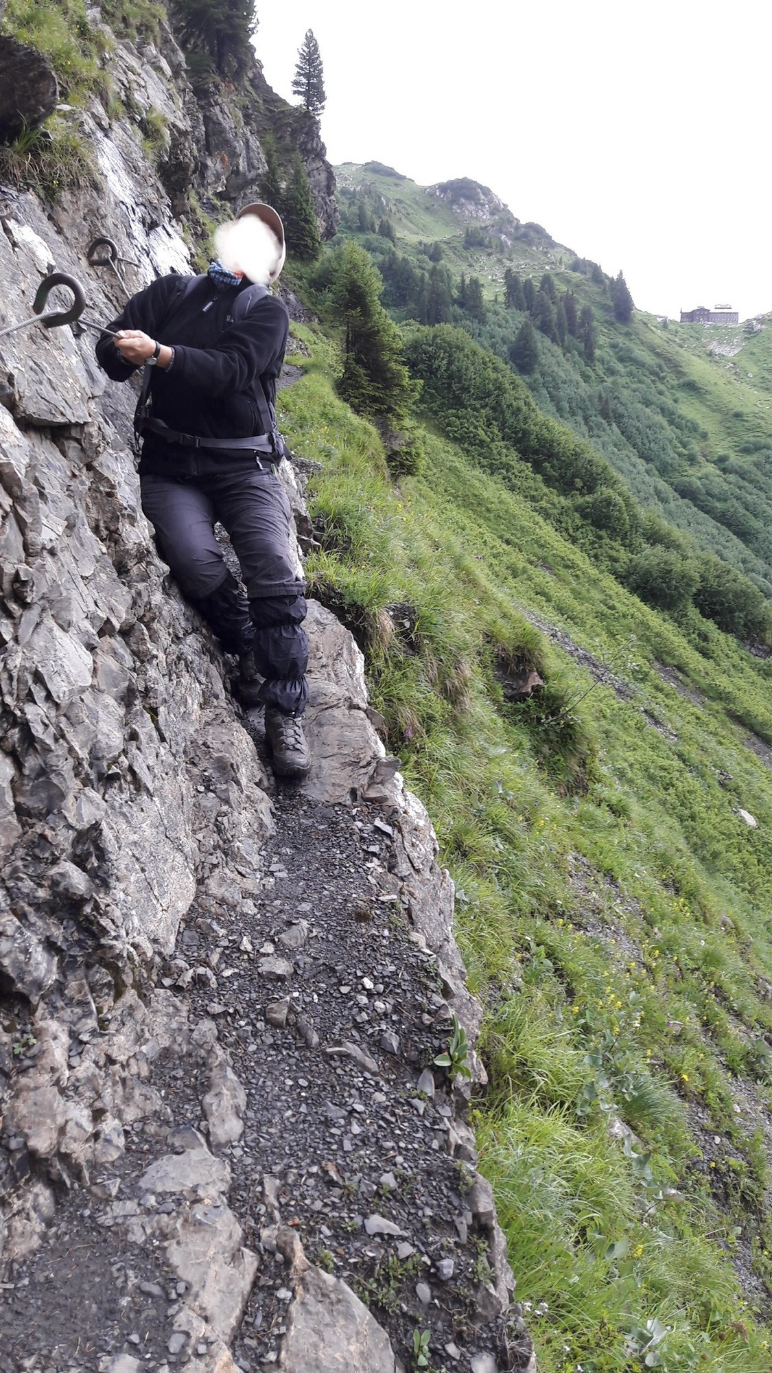 Ein schmaler Weg an einer bergflanke, eine Wanderin balanciert mit Hilfe der seilversicherung auf dem schmalen weg.