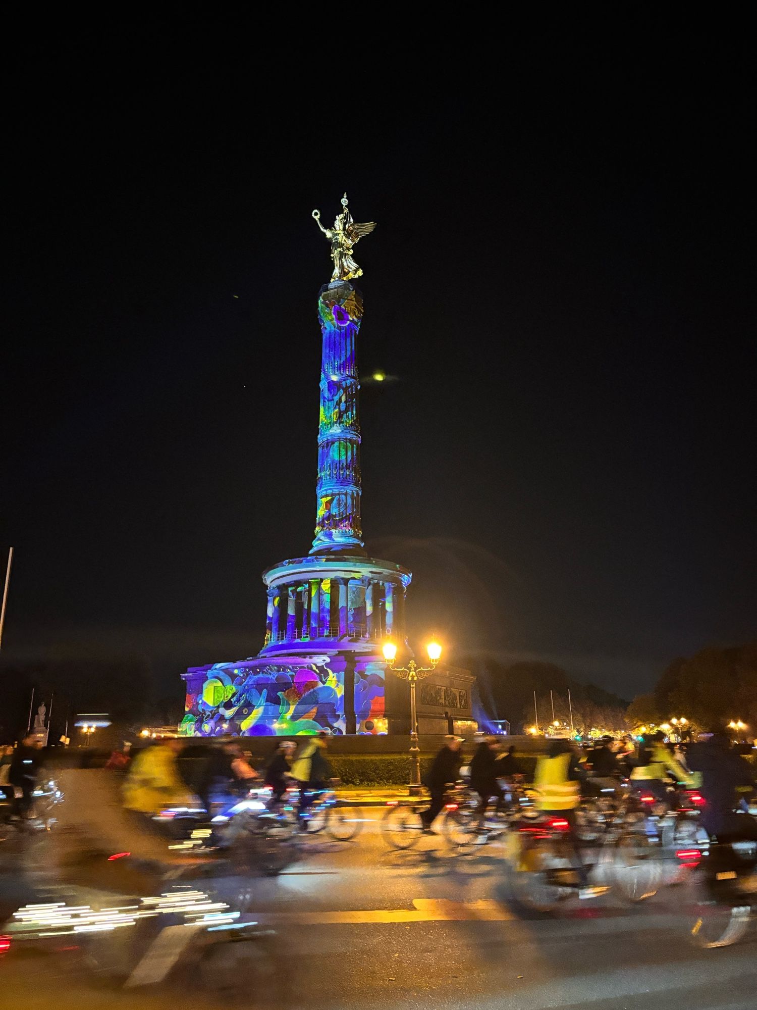 Die bunt angestrahlt. Kate Siegessäule wird von Fahrradfahrern umfahren.