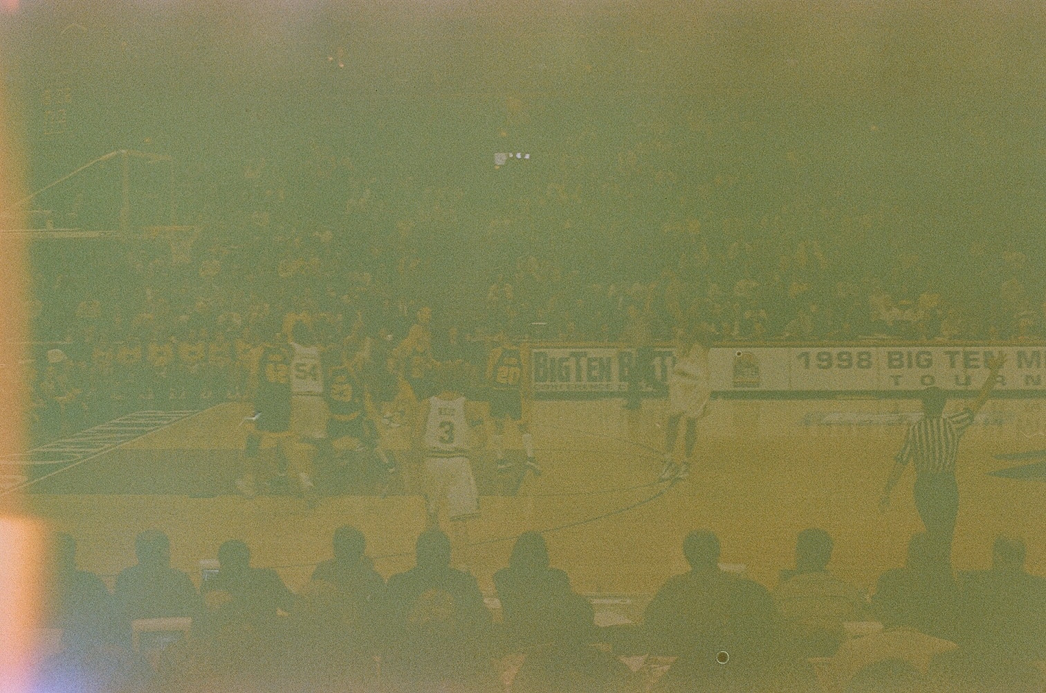 very expired, grainy photo of michigan playing iowa in basketball with 1998 big ten tournament banners visible