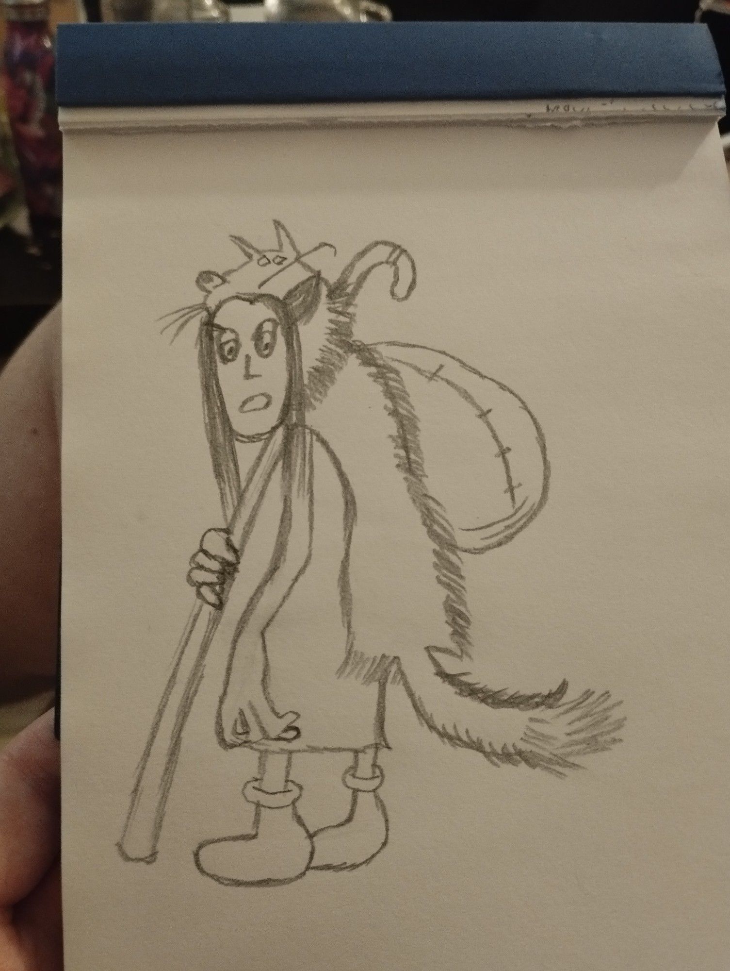 Dessin d'un druide portant un manteau en peau de loup et sa canne.
Il est de 3/4 et regarde vers nous