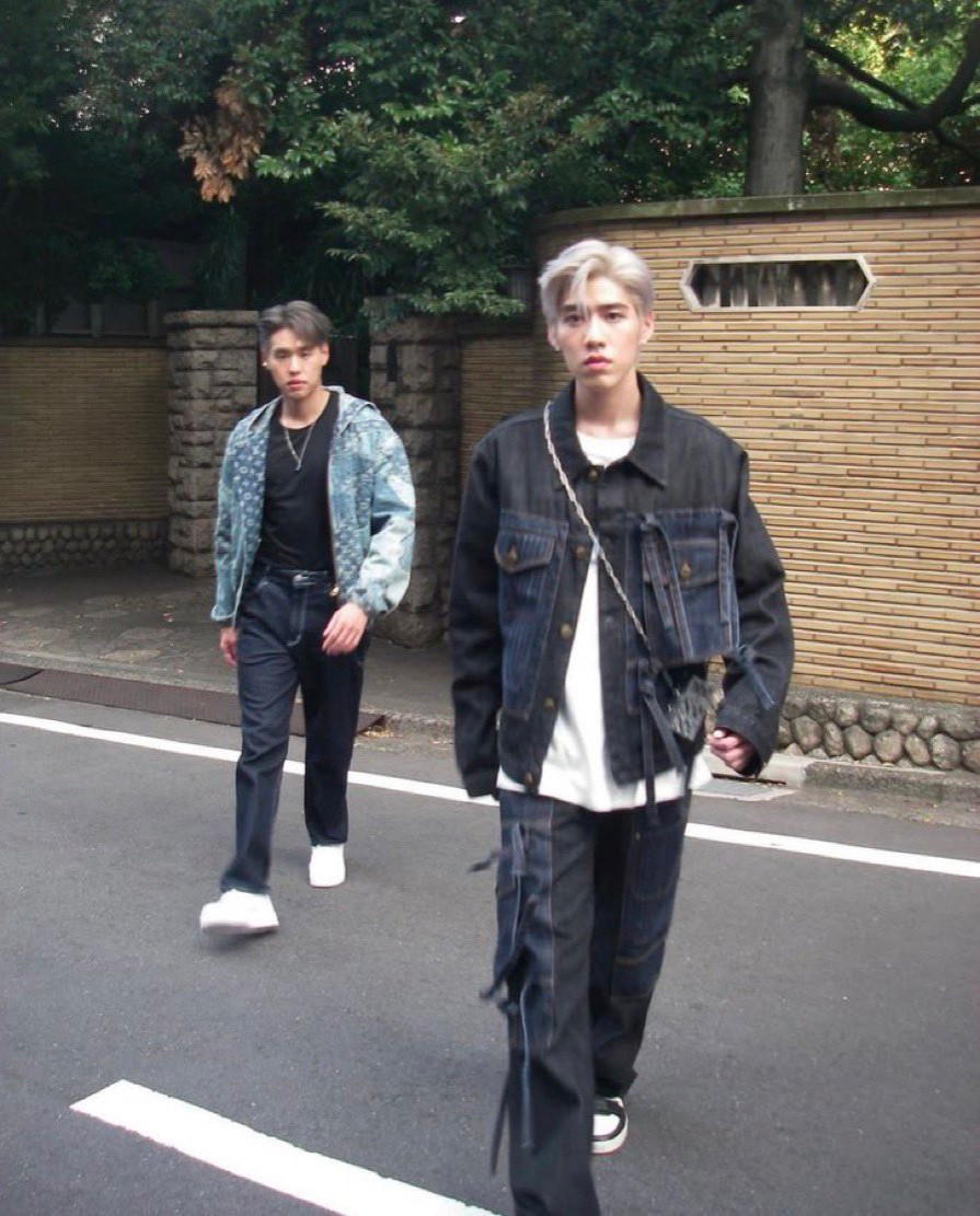 Billkin (in the back) and PP Krit(in the front) looking straight at the camera while walking down a street in Japan.