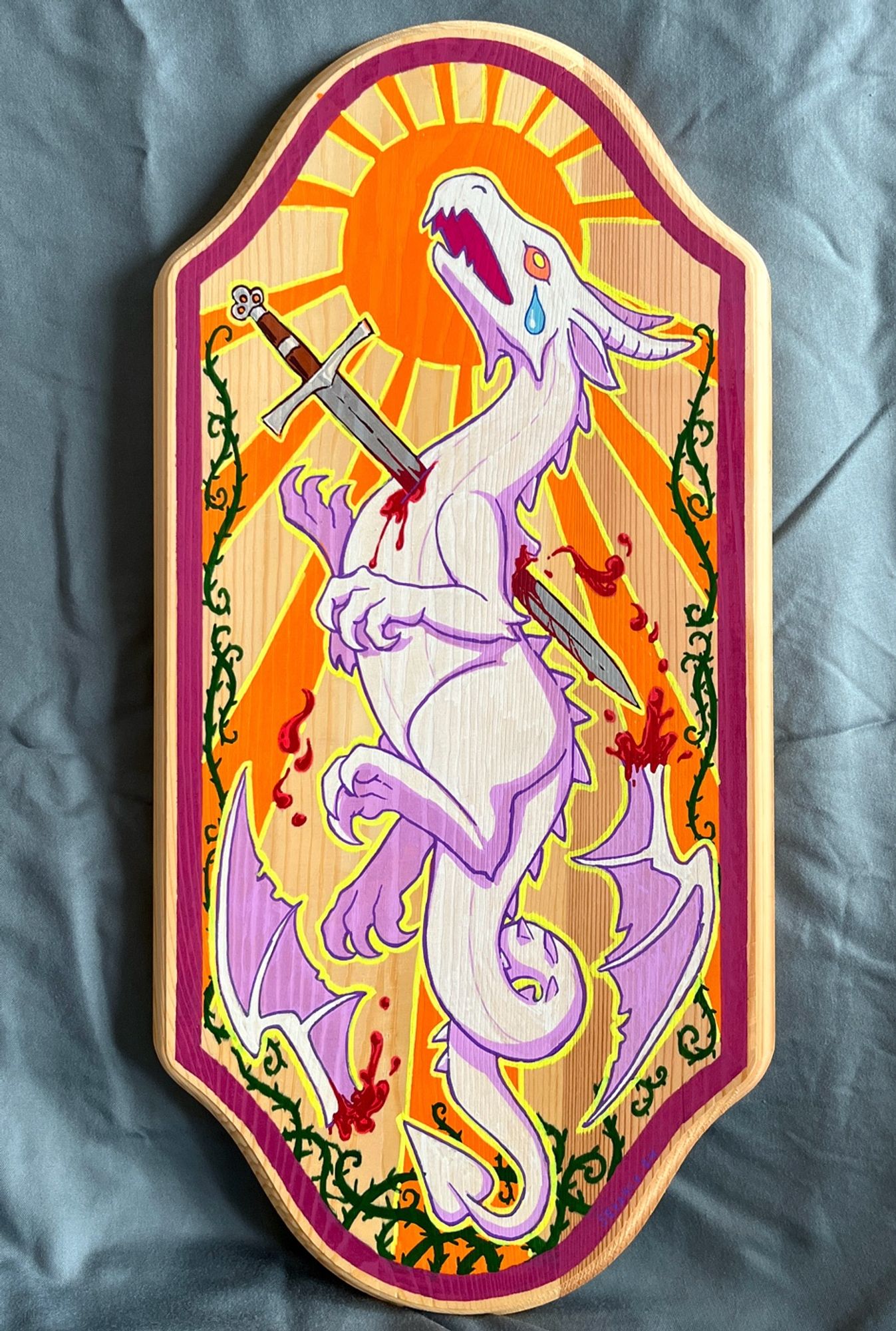 Photo of tall wooden plaque with painting of a heraldic-esque white dragon with a longsword plunging through its chest, bleeding, and with cut wings falling to the sides. The backdrop features an orange sun with long beams and ornate dark thorny vines twisting from the bottom up the sides. All within a raspberry colored frame.