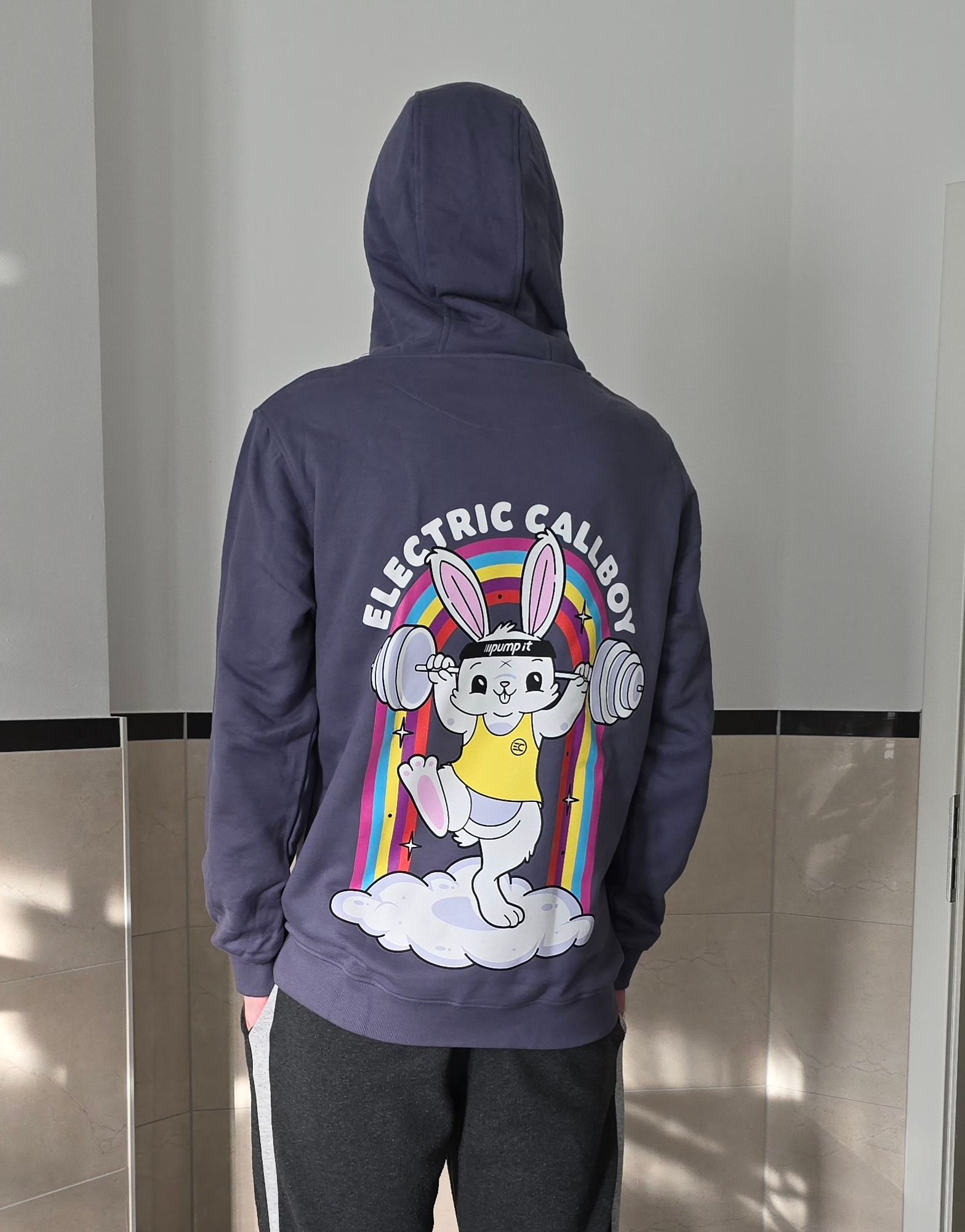 Person looking at the wall, wearing a hoodie that states "Electric Callboy".
The print is a bunny training, and a rainbow in the back, standing on a cloud