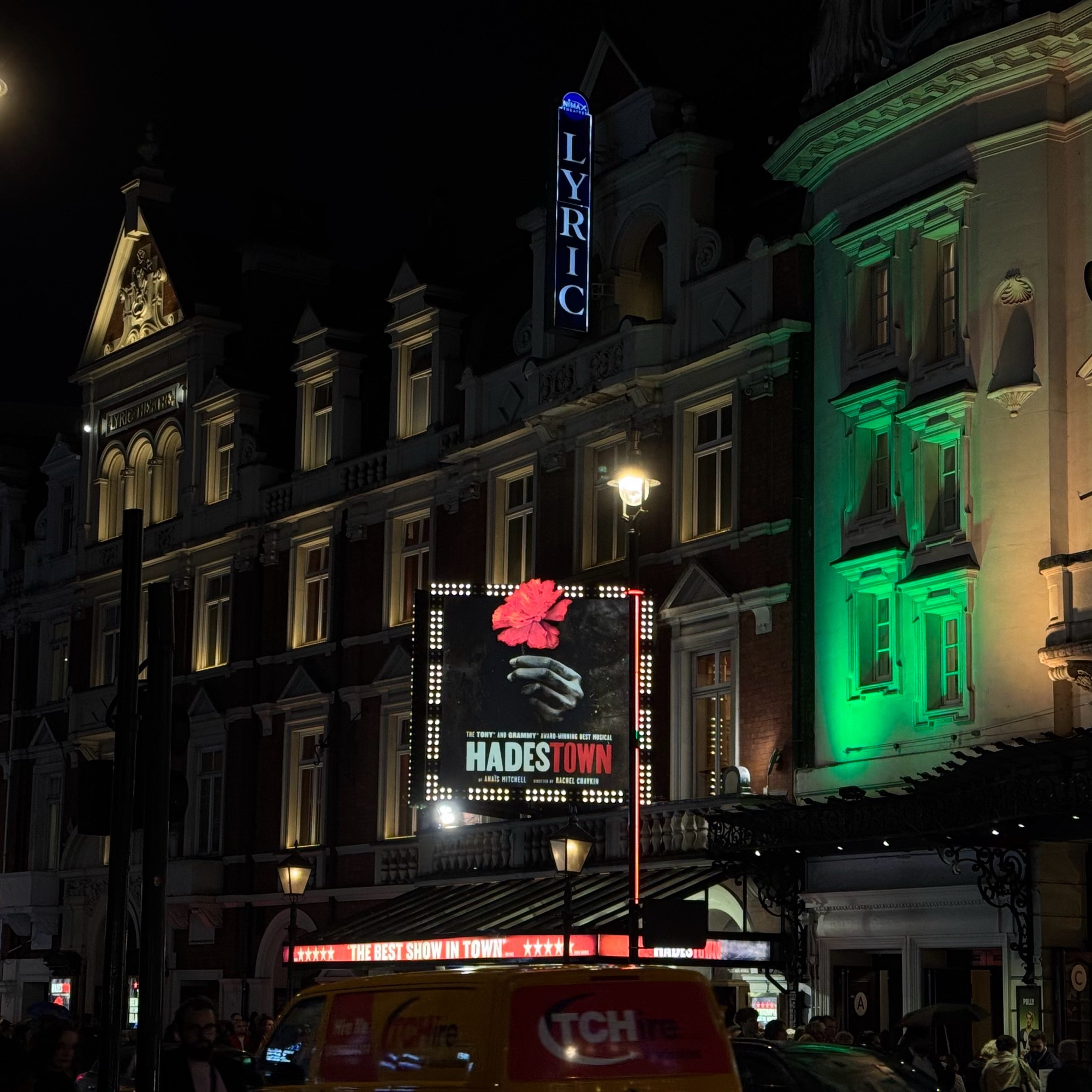 Outside of a west end theatre. A billboard for Hadestown is in lights.