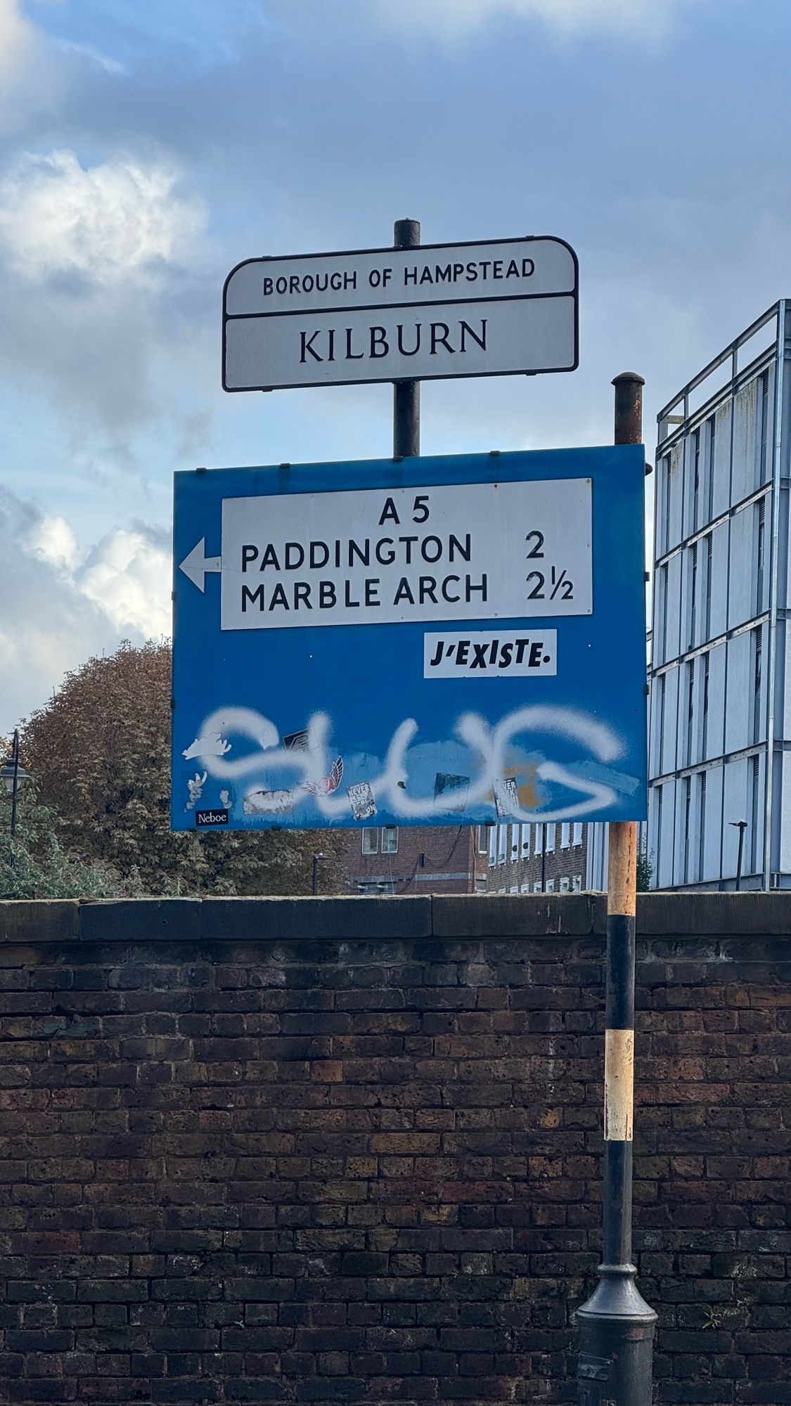 A heavily graffitied London road sign pointing to the A5. Paddington 2 miles, Marble Arch 2 ½.