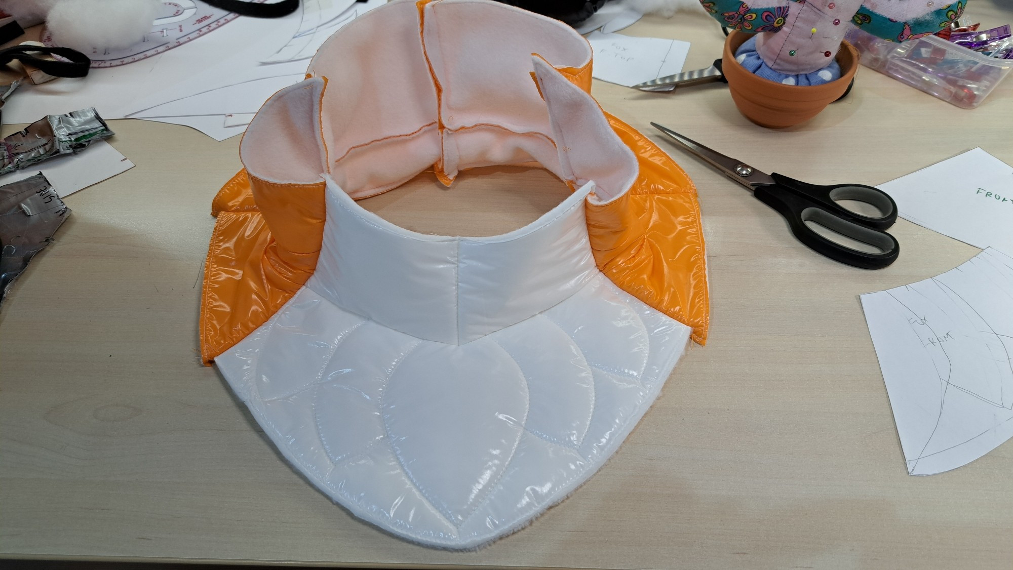 The neck section of a fursuit head made of orange and white nylon.  The front has a tufted pattern embroidered into it.