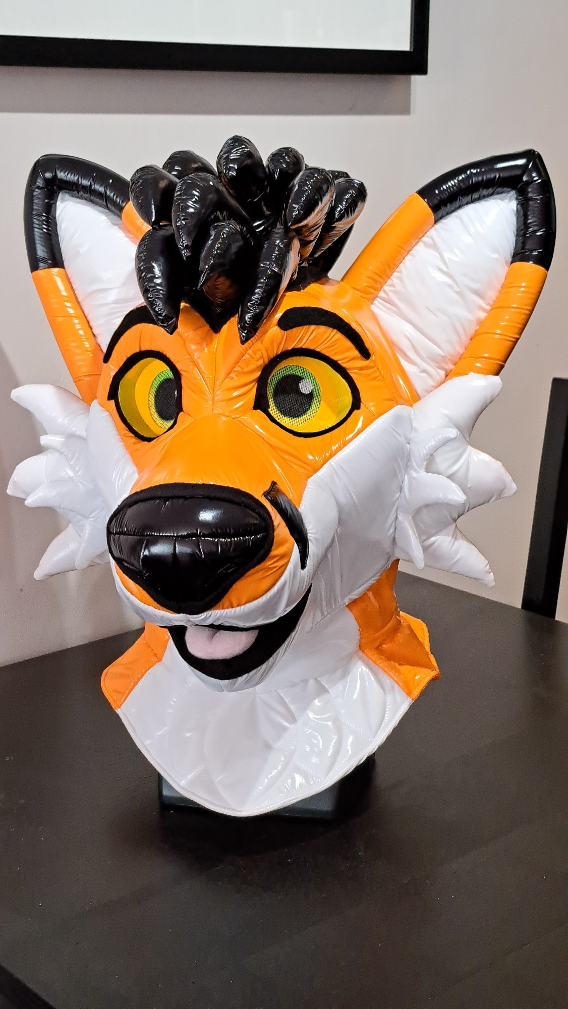 Flynn, the orange nylon fox. Made of shiny orange and white nylon on a foam headbase, with shiny black spiky hair.