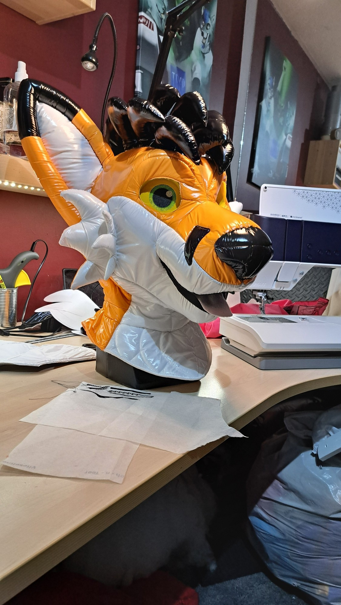 An orange and white fox fursuit head made of shiny nylon fabric.  Just finished sewing on the shiny black tufty hair.