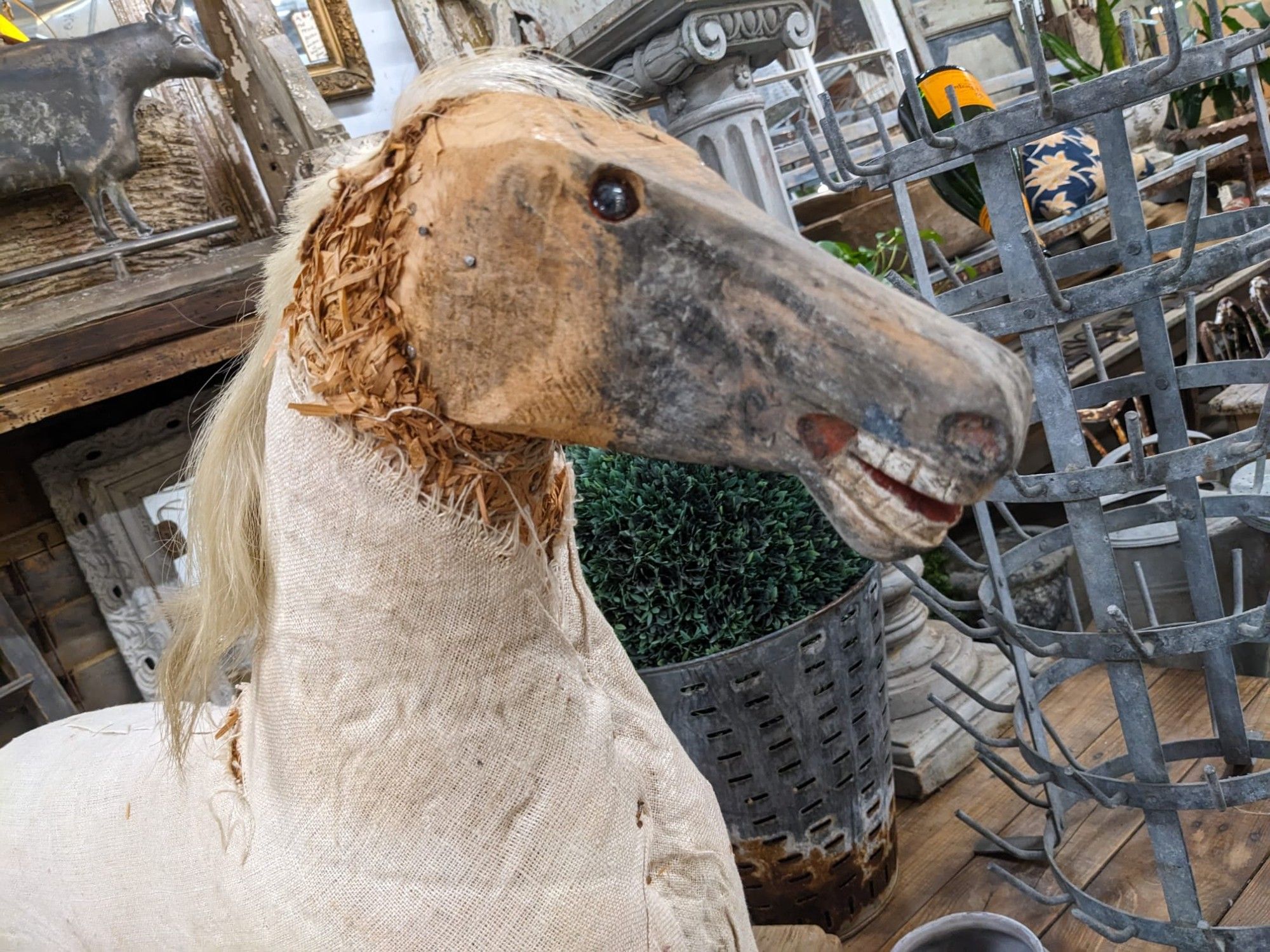 A rocking horse. The teeth are bared, and the glass eyes are beady and sunken. The paint has worn completely off the face, and what appear to be padding has split and frayed around its head and neck. A lock of what could be horse hair but looks disturbingly like human hair clings to the skull.