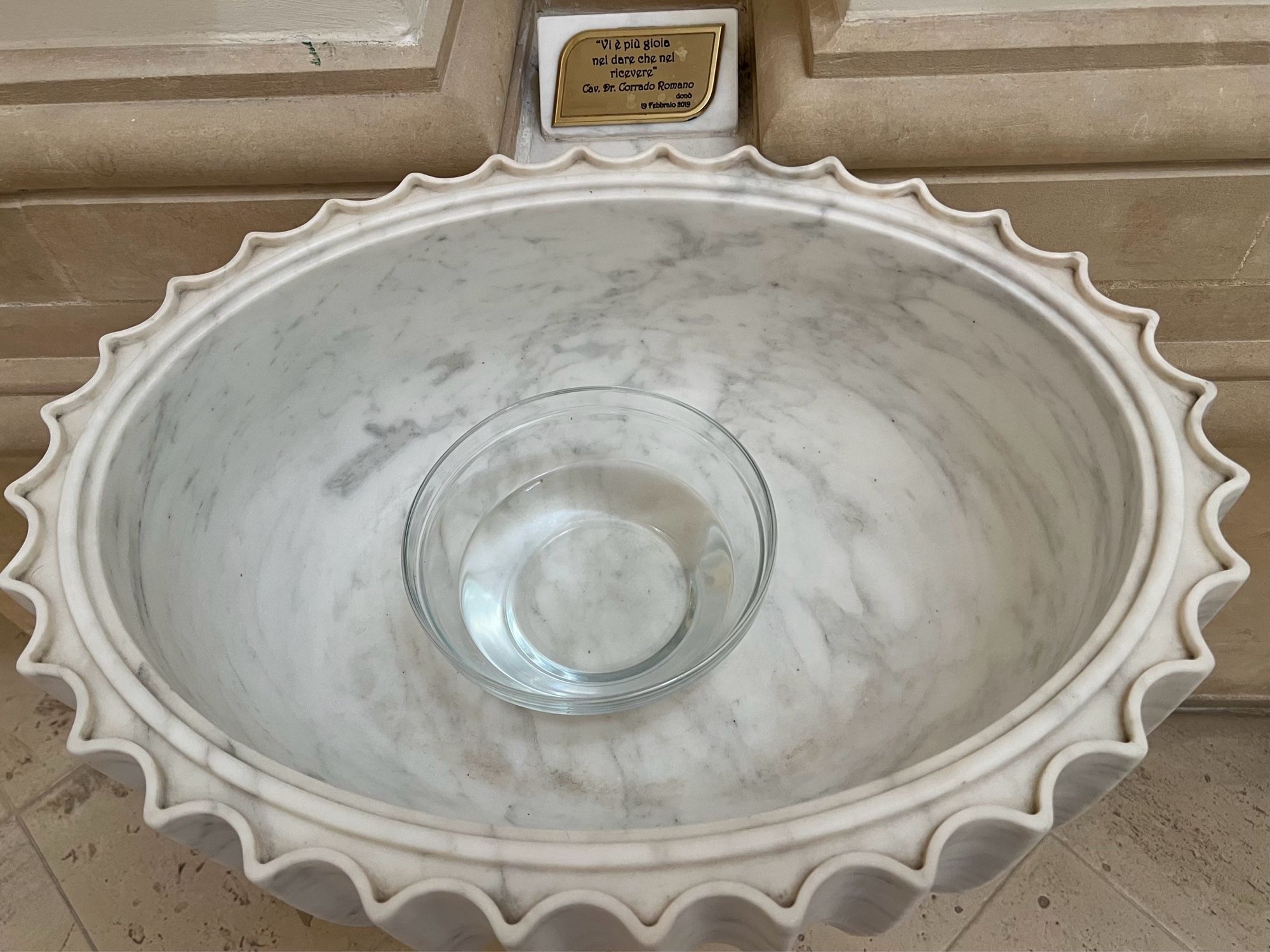 A glass bowl containing holy water in a Baroque marble font in Noto, Sicily.