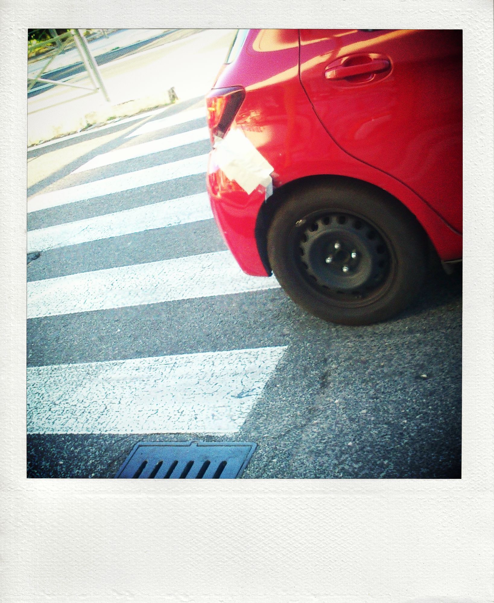 Fake instant photo of a red car with a bandaged rear bumper leaving a pedestrian crossing. Sony Ericsson Xperia MiniPro, edited with Toycamera Analogcolor to achieve the polaroid effect.