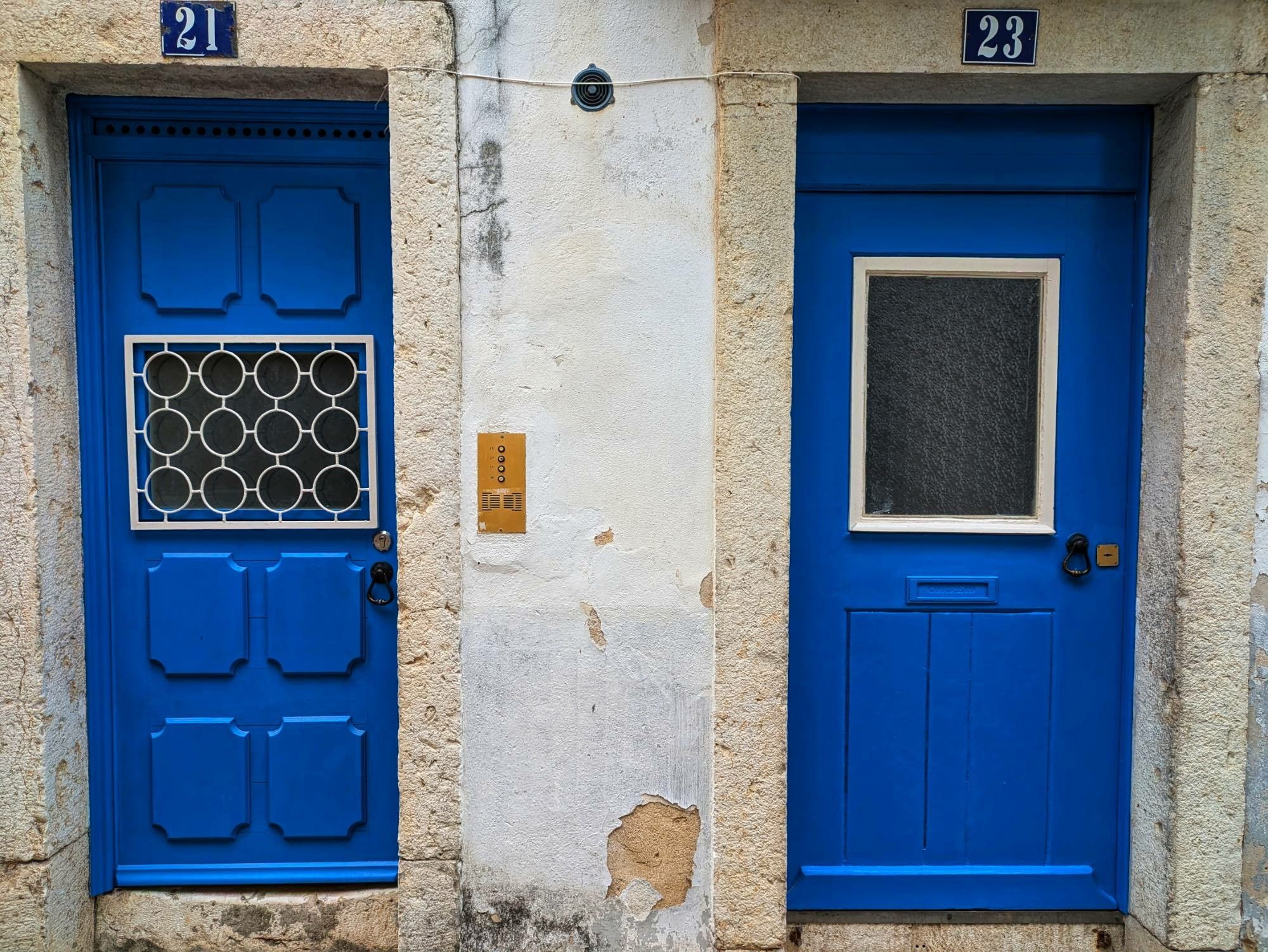 zwei leuchtend blaue Haustüren nebeneinander.
Die Fenster in den Türen sind unterschiedlich breit und hoch. Das linke Fenster ist vergittert