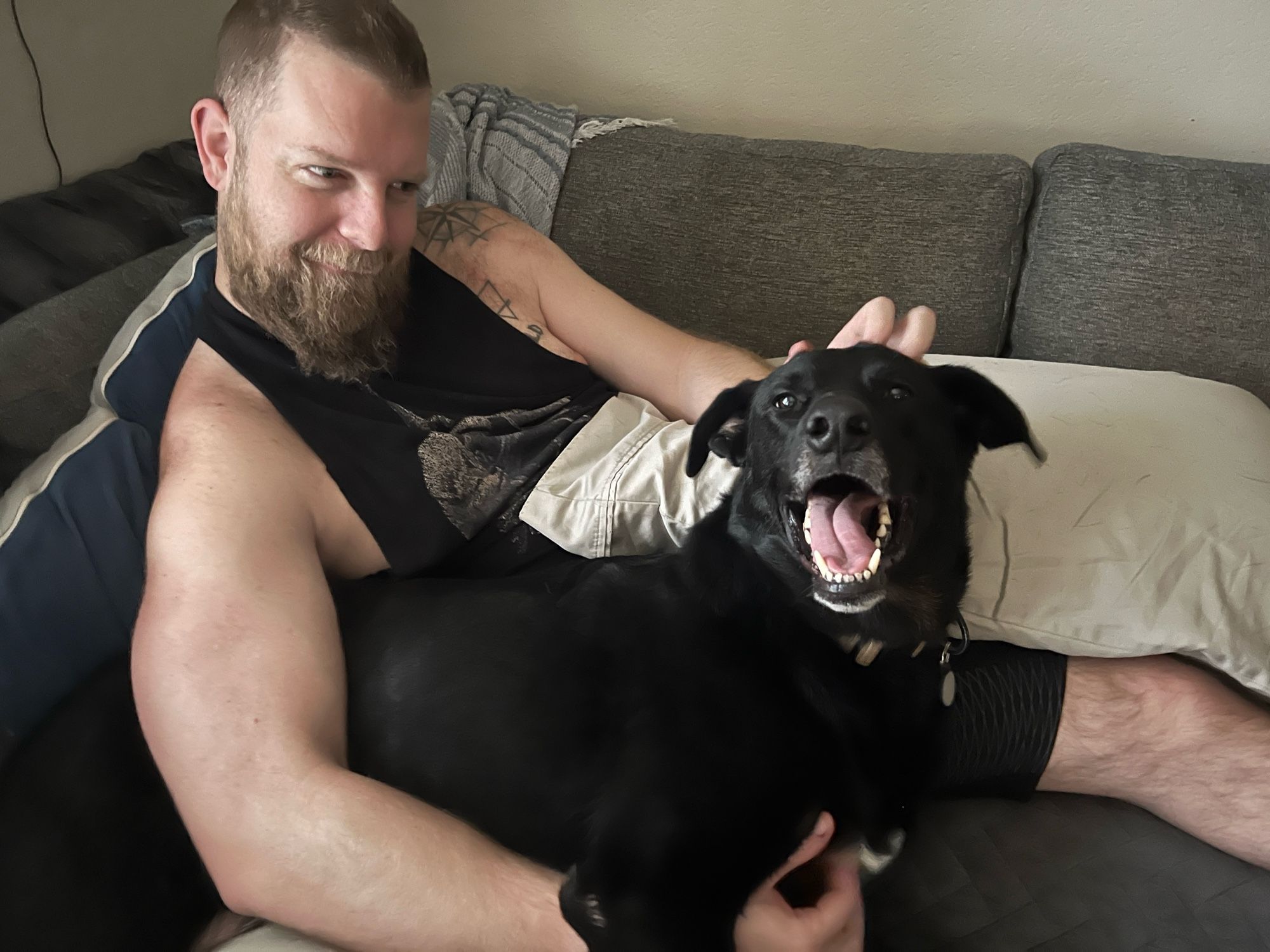 Me and my dog Rock, a black German Shepherd/Rottie mix, I am indeed making a slightly crazy side eye smile at Rock and he has a goofy open mouth grin with I pet him on the chest and head