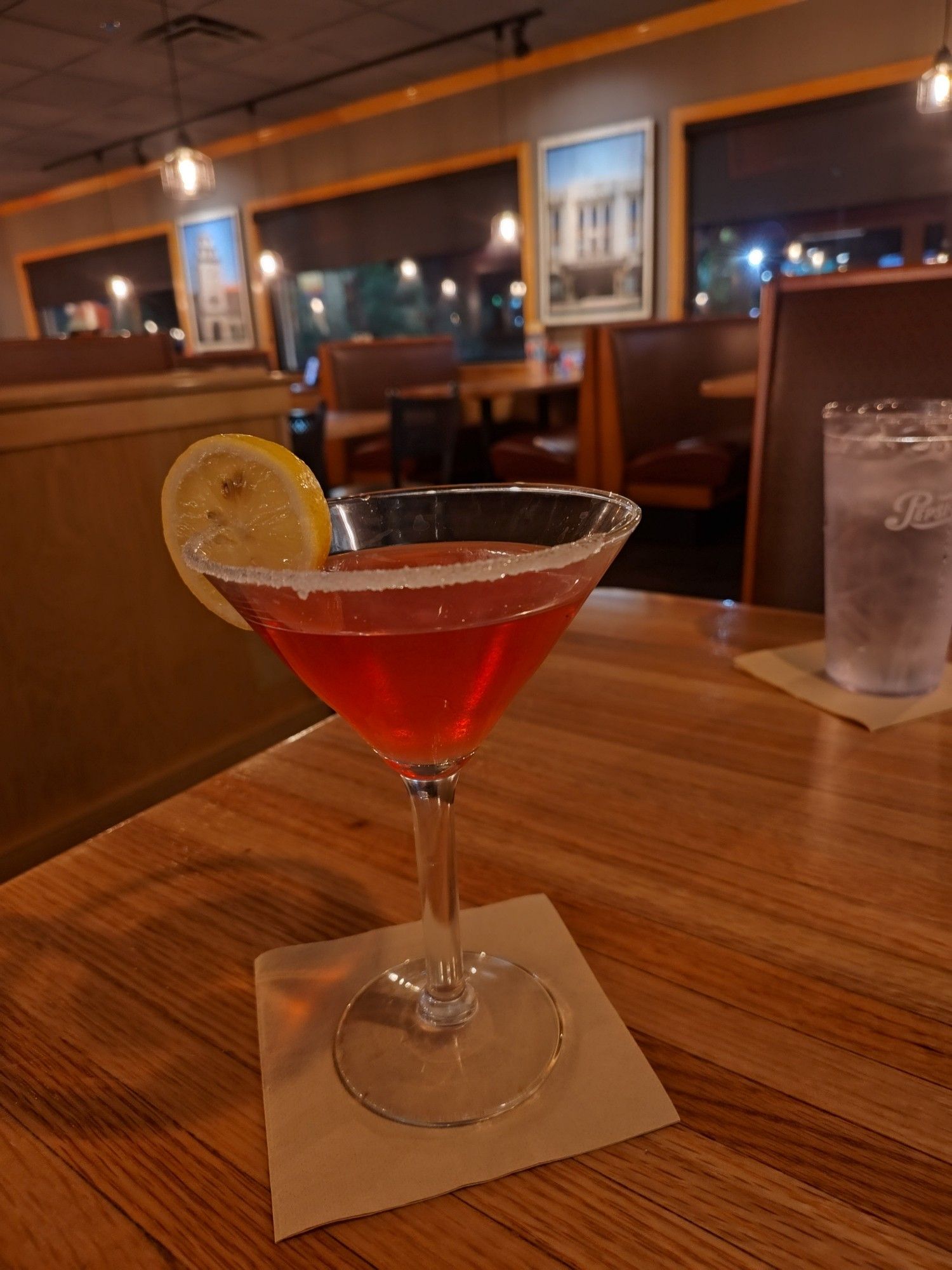 A light pink beverage in a  sugar-rimmed martini glass with a lemon slice