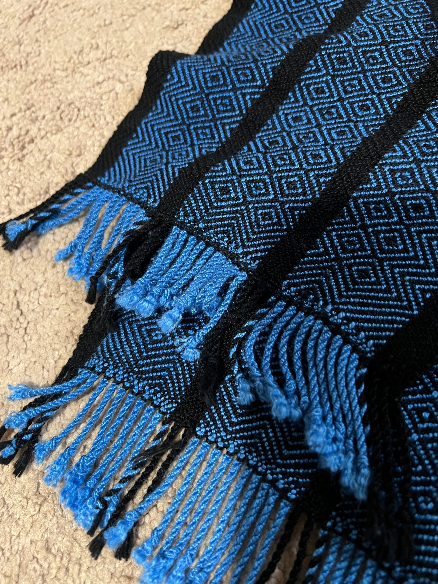 Detail shot of blue and black striped scarf showing black diamond twill pattern and twisted fringe with black hem stitching