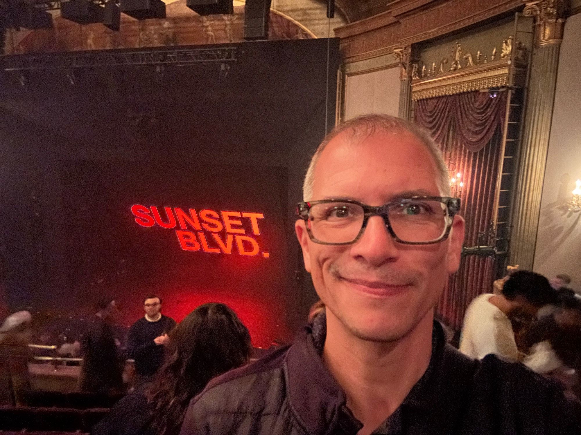 Chris in the theater after the show. A giant Sunset Blvd. image in bright right is displayed on the stage.