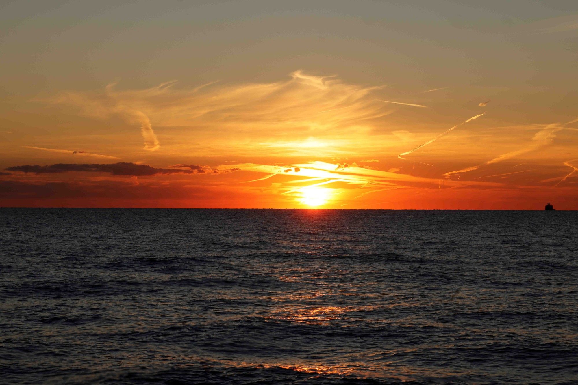 Wide shot of Sun rising from Lake Michigan. There is a band of orange skies, grey above. Water intake crib of to the right. Lake Michigan is mildly choppy.