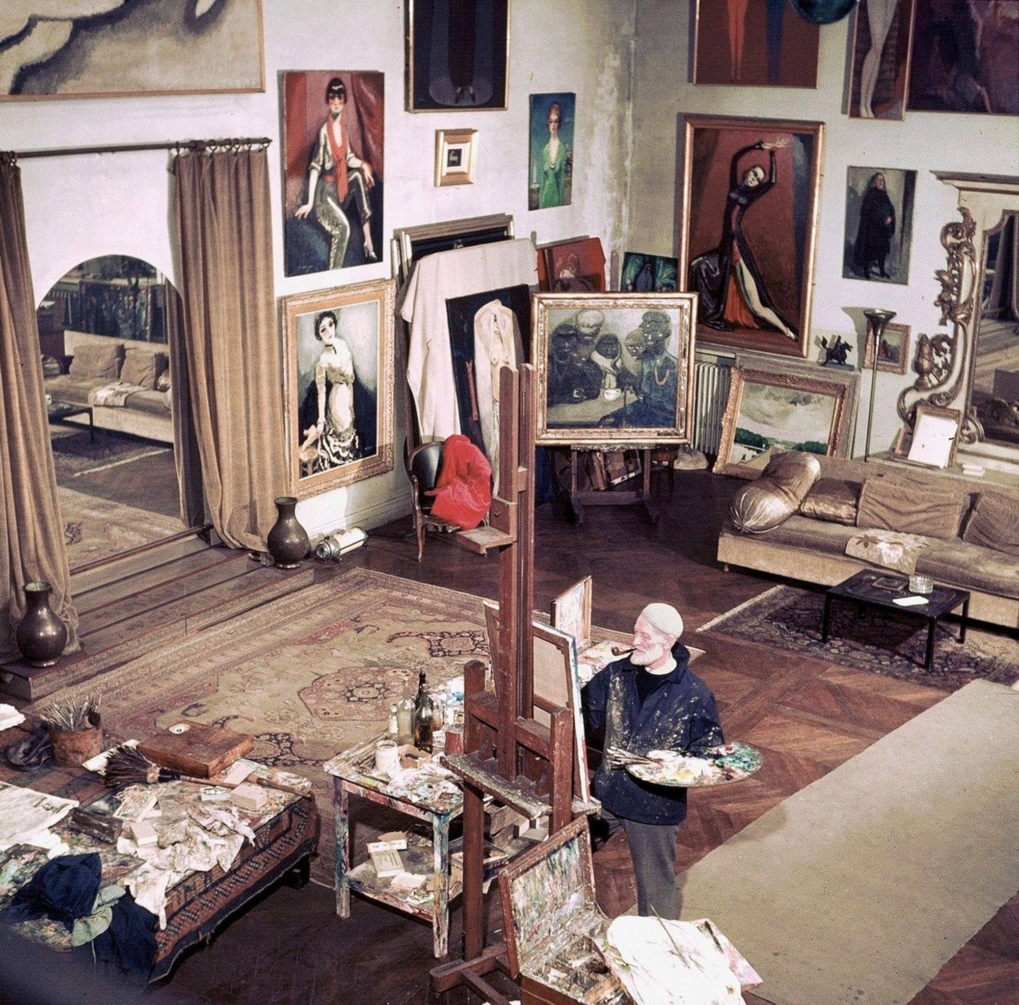 Kees Van Dongen dans son atelier en train de peindre, grand tapis et peintures aux murs

–––––

1959

René Vital