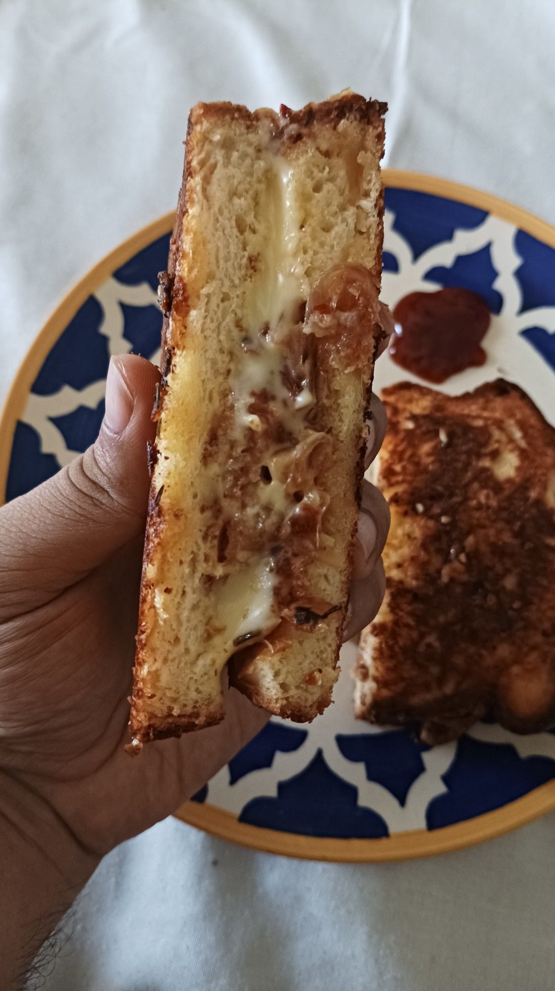 Holding half a sandwich and showing the cross section. You can see bread, japanese mayo, cheese (melted) and chicken patty.

There's another half a slice on the plate below and some ketchup. 

The plate is ceramic with blue patterns in the circumference and a yellow line outside.