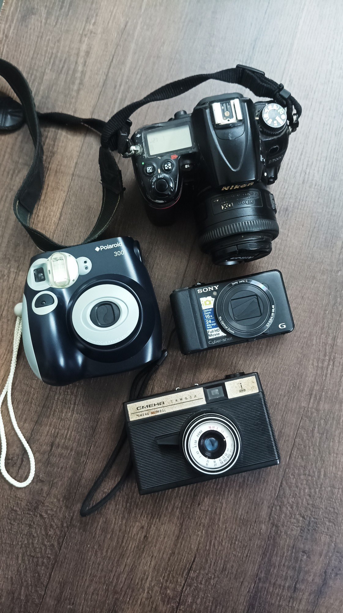 4 different cameras on a table. We use them based on what the usecase is. 

A nikon d7000 with 35mm prime. (Top)
Polaroid on left and sony pount and shoot on the right.
A Smena Symbol (from the late 70s) Lomo camera.