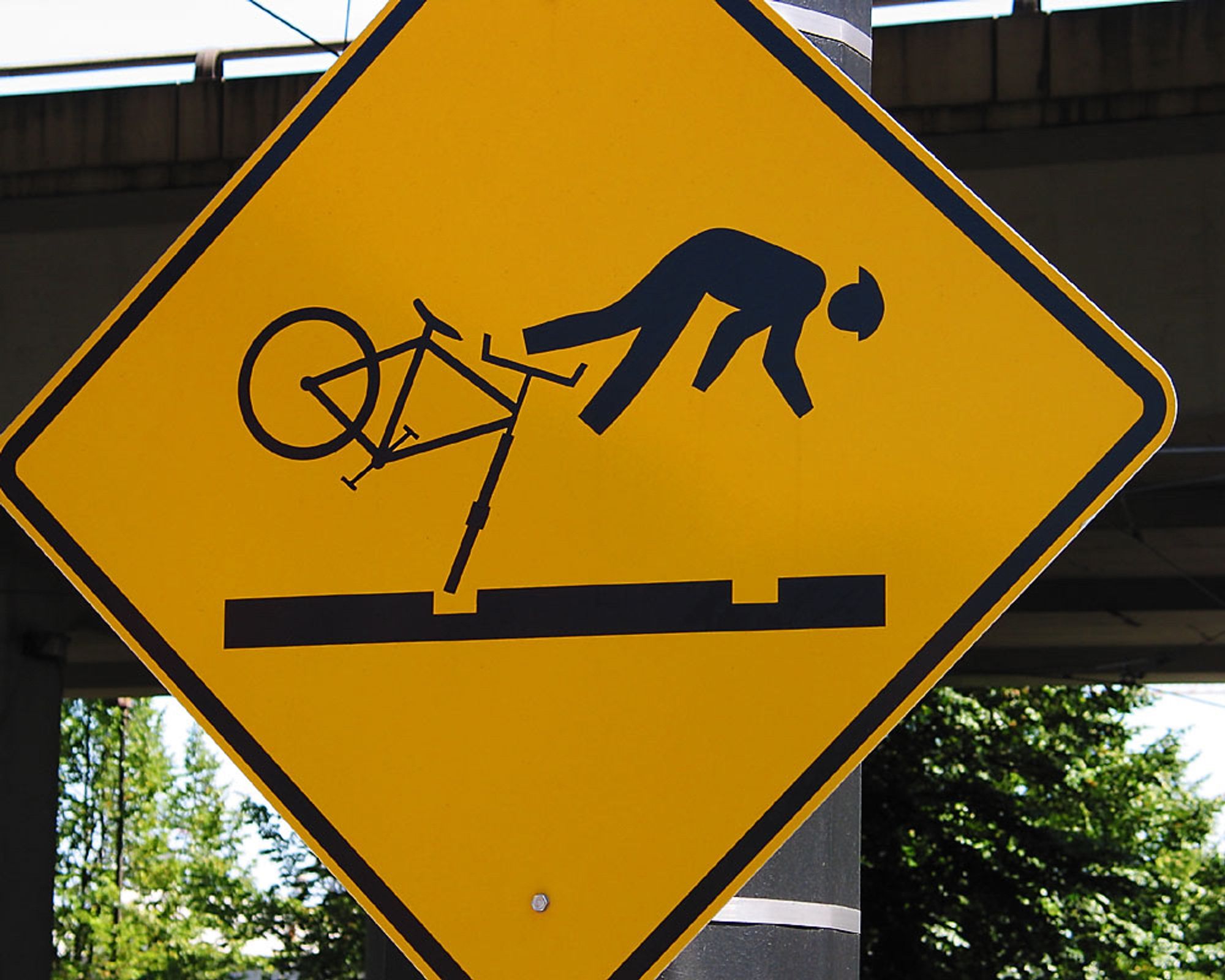 A warning sign of a cyclist ejecting off their bike due their tire being stuck in a street car track