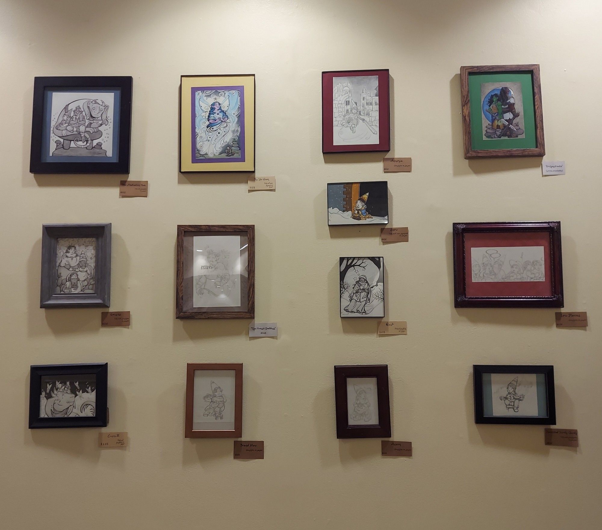 A photograph of a gallery wall with a grid of 13 framed images, all featuring various faerie and fantasy characters.