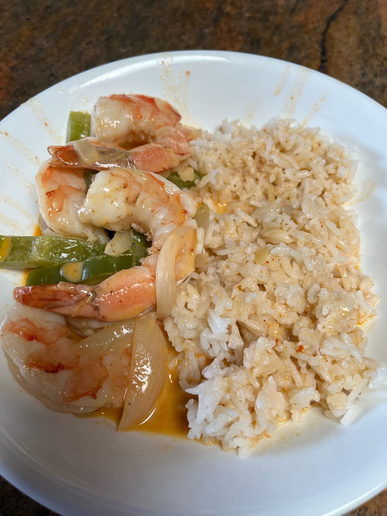 A saucer with shrimp, green capsicum, and sliced onion on one side and a pile of jasmine rice dressed in red curry sauce on the other.