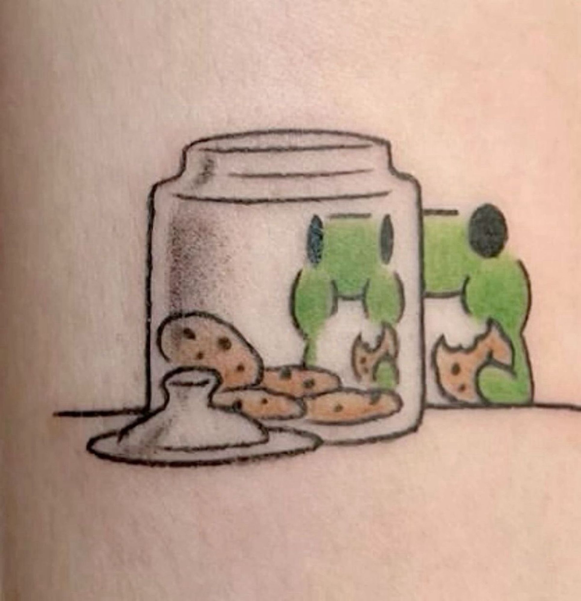 tattoo von kl frosch der vor keksglas sitzt ubd 1 keks isst durch das glas ist sein gesicht ganz kl