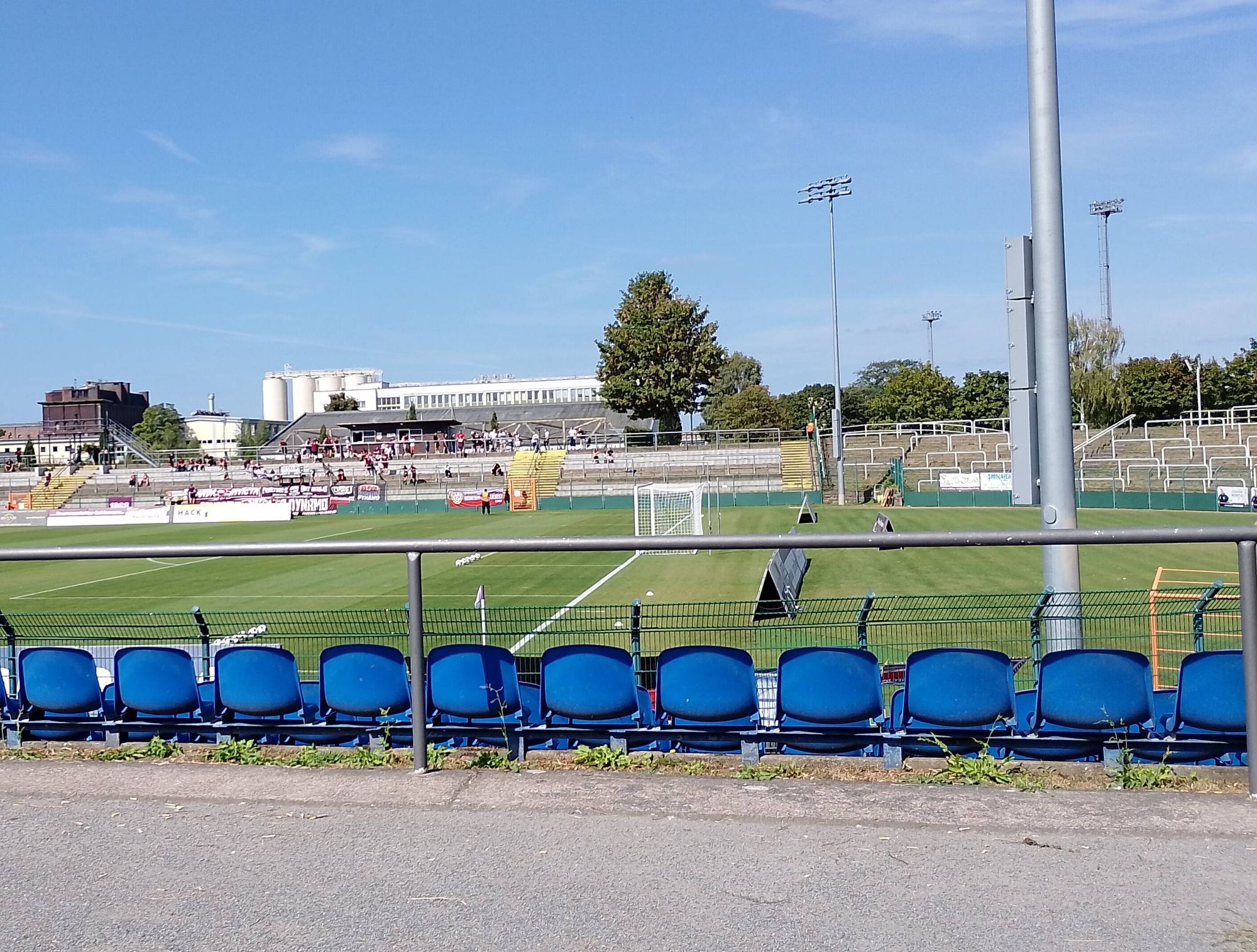 Eine Reihe blauer Sitzschalen, dahinter Spielfeld und Gegentribüne des Sportforums Hohenschönhausen. Und viel blauer Himmel