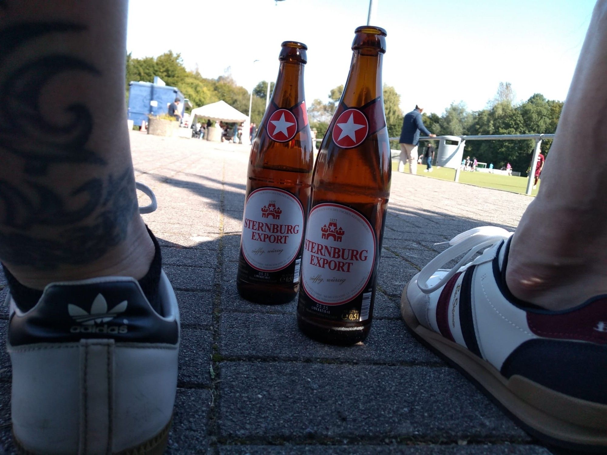 Bier und Sneaker. Im Hintergrund ein Fußballplatz