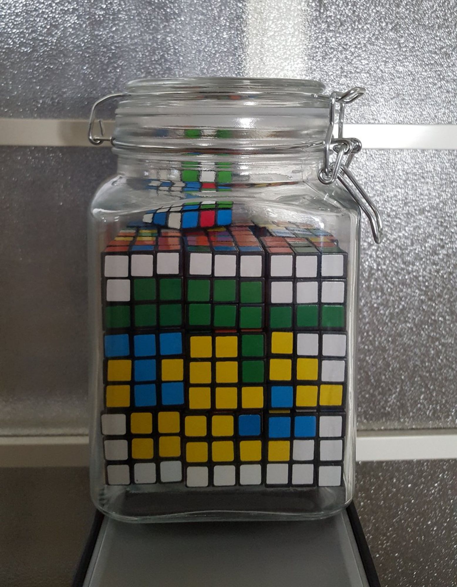 9 small Rubik's Cubes in a jar arranged to form pixel art of Luigi with blue hair.