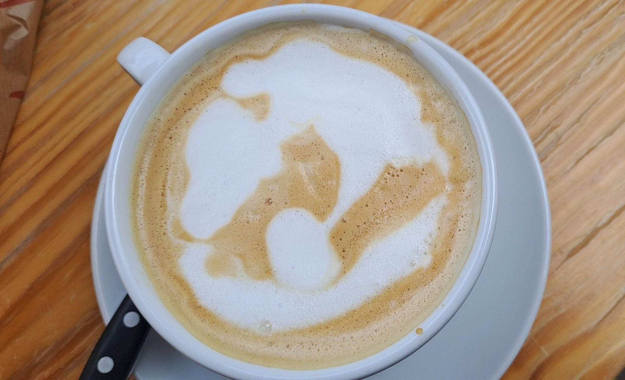 A coffee with milk foam forming a map of the World, over a wood table