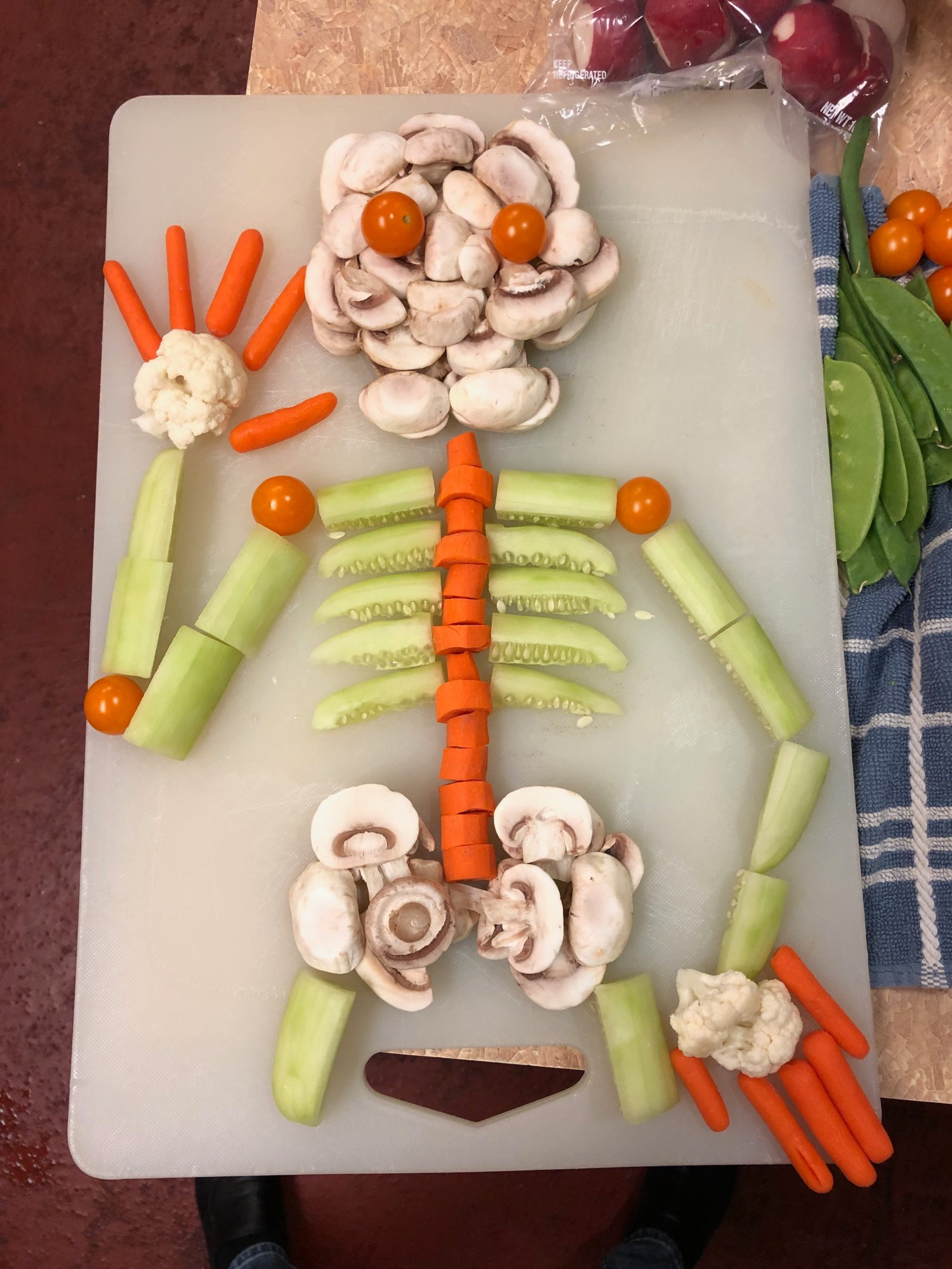 Crudités in the shape of a skeleton: mushroom slices, cherry tomatoes, cucumber slices, sliced and baby carrots, cauliflower florets.