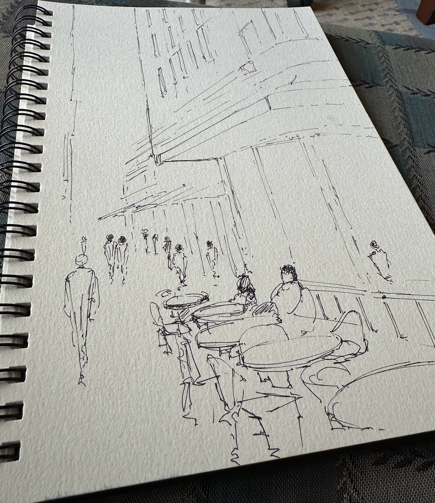 Début de dessin d’une rue. Un café en terrasse avec des silhouettes dans le fond 