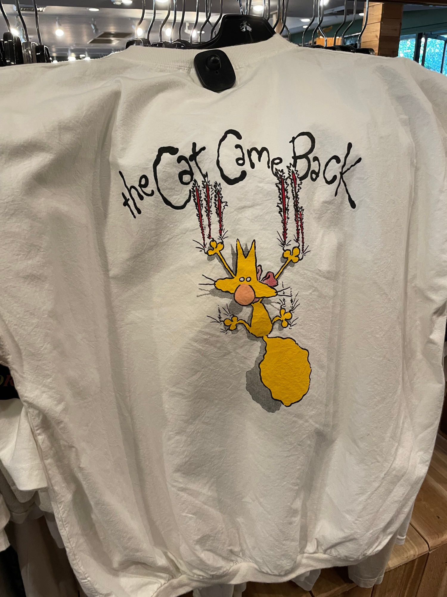 the back of a white t-shirt, hanging on the rack in a vintage shop, shows a promotional illustration for The Cat Came Back (1988).