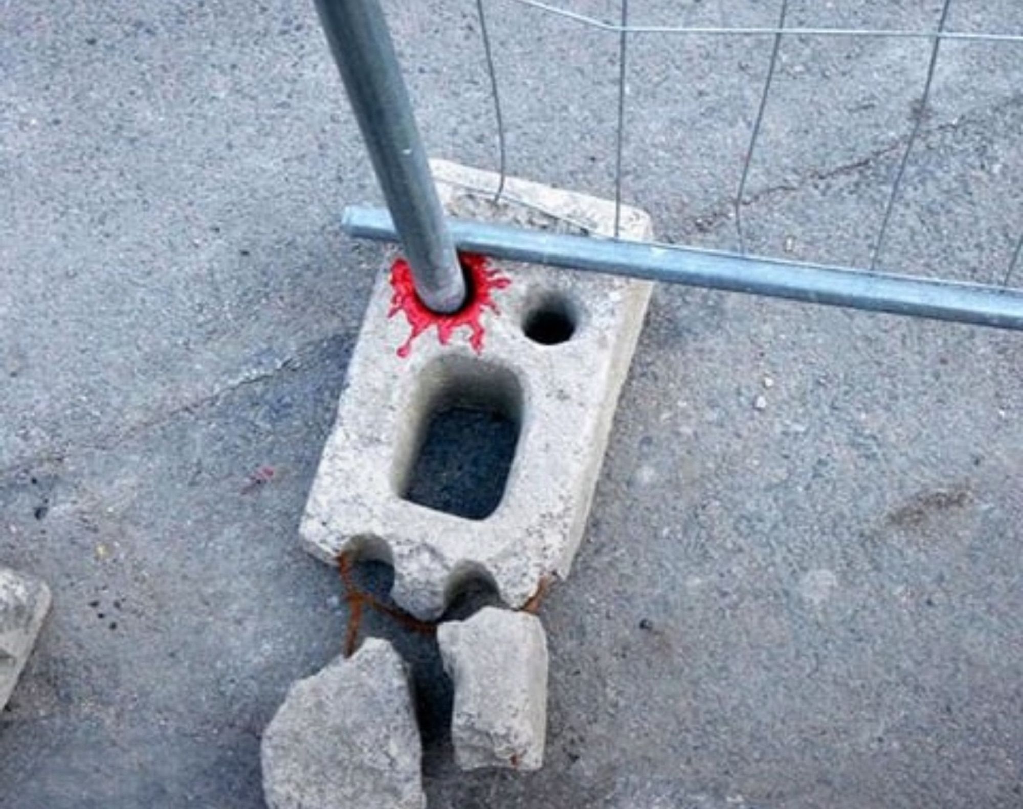 A concrete block holding a metal railing. Someone has ringed one of the circles with red making it appear that it’s got a bloody ringed eye.