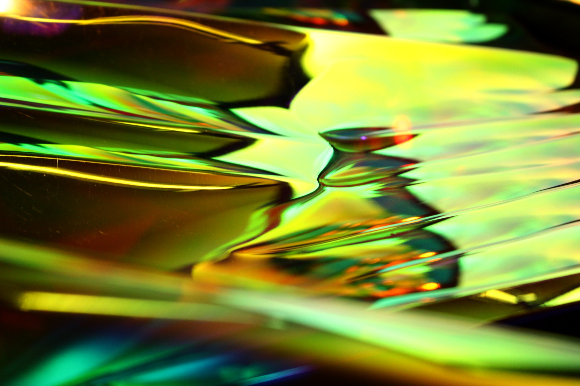 Abstract photograph of an iridescent, warped vinyl sheeting over a scanner. Primarily yellow with teal edges and reddish shadows.