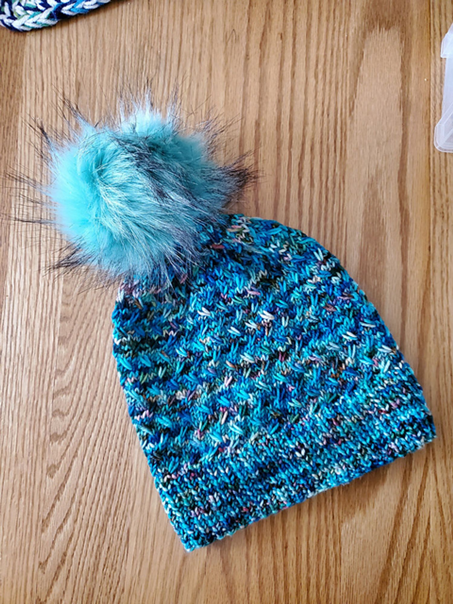 Hat knitted for myself in variegated blue yarn that uses slip stitch texture to highlight the changes in colors. It is topped with a teal pompom flecked with black.