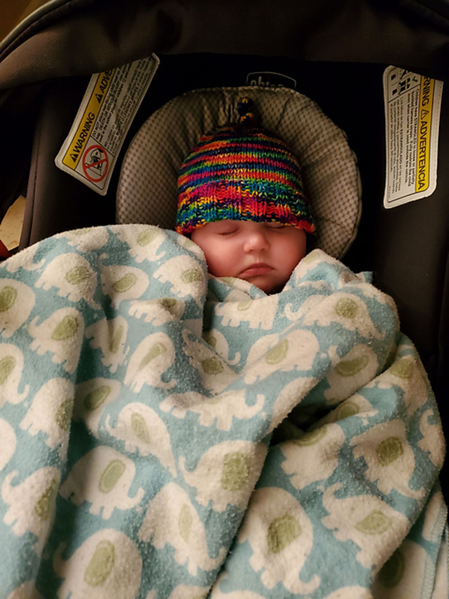 A sleeping baby in a carseat, with a neon variegated hat on her head. This was the first thing I let myself knit hopefully for her when I was pregnant, made from leftover scraps of a hat knit for a friend.