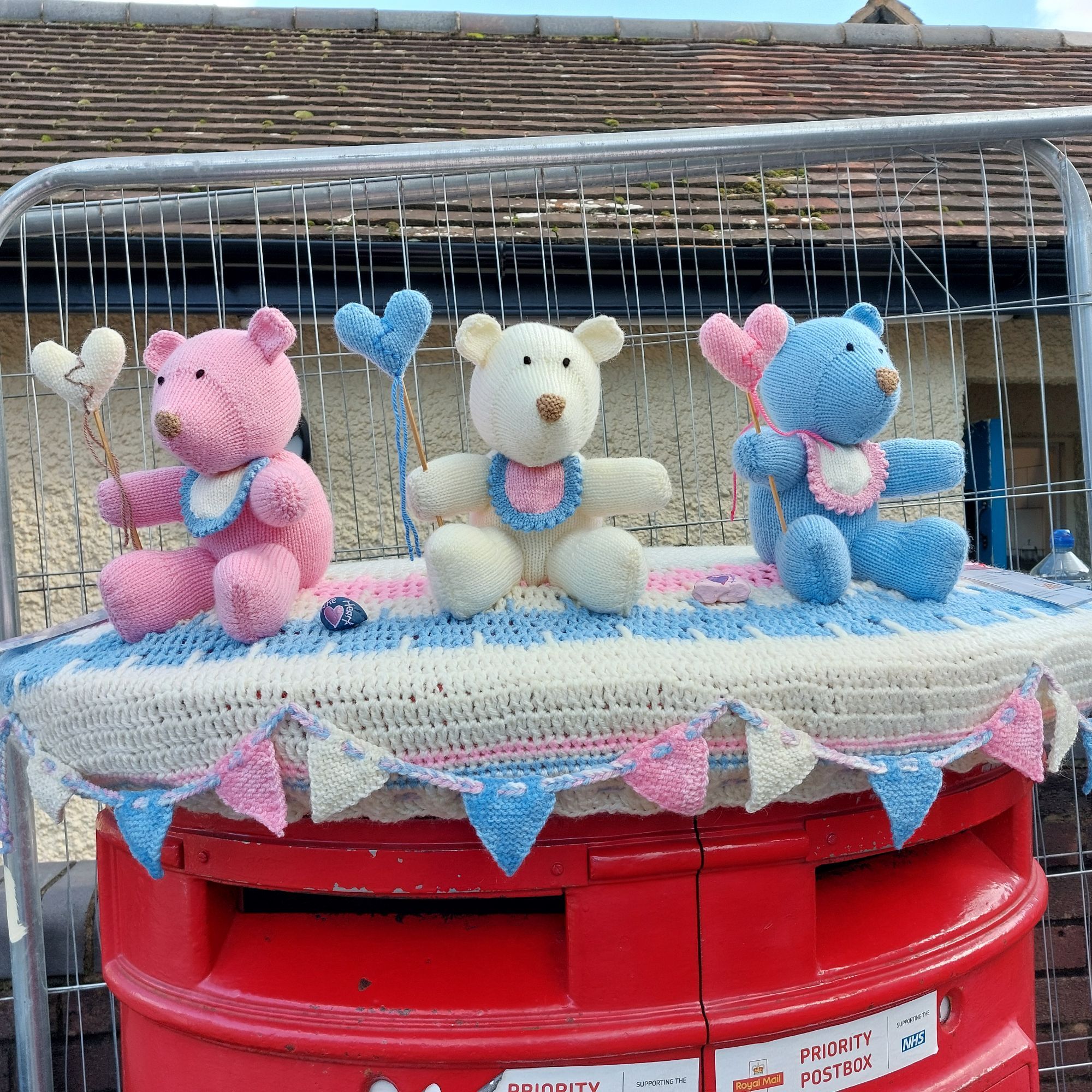 Three crochetrd teddy bears in pink, cream and blue, as a yarnbombing postbox lid.