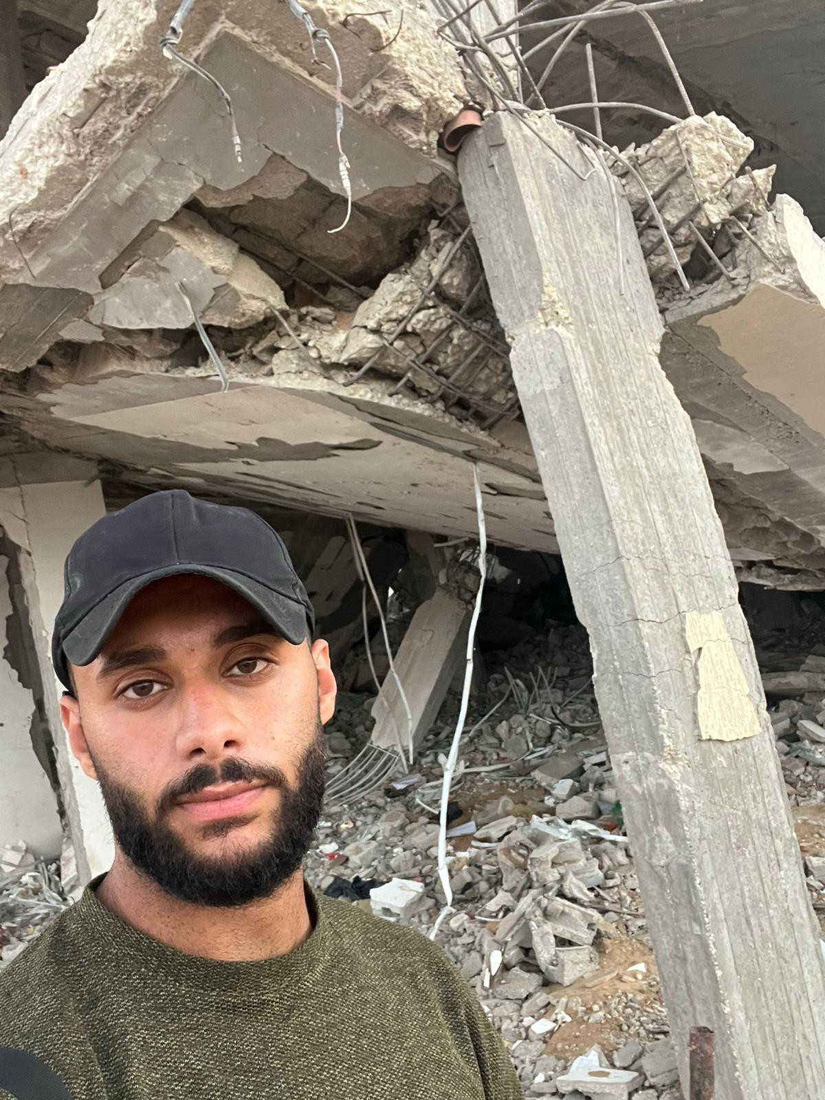 Close-up in front of a demolished apartment: shattered concrete, dangling wires, exposed steel. He looks hungry and worn out—but still standing. Please help him survive.
