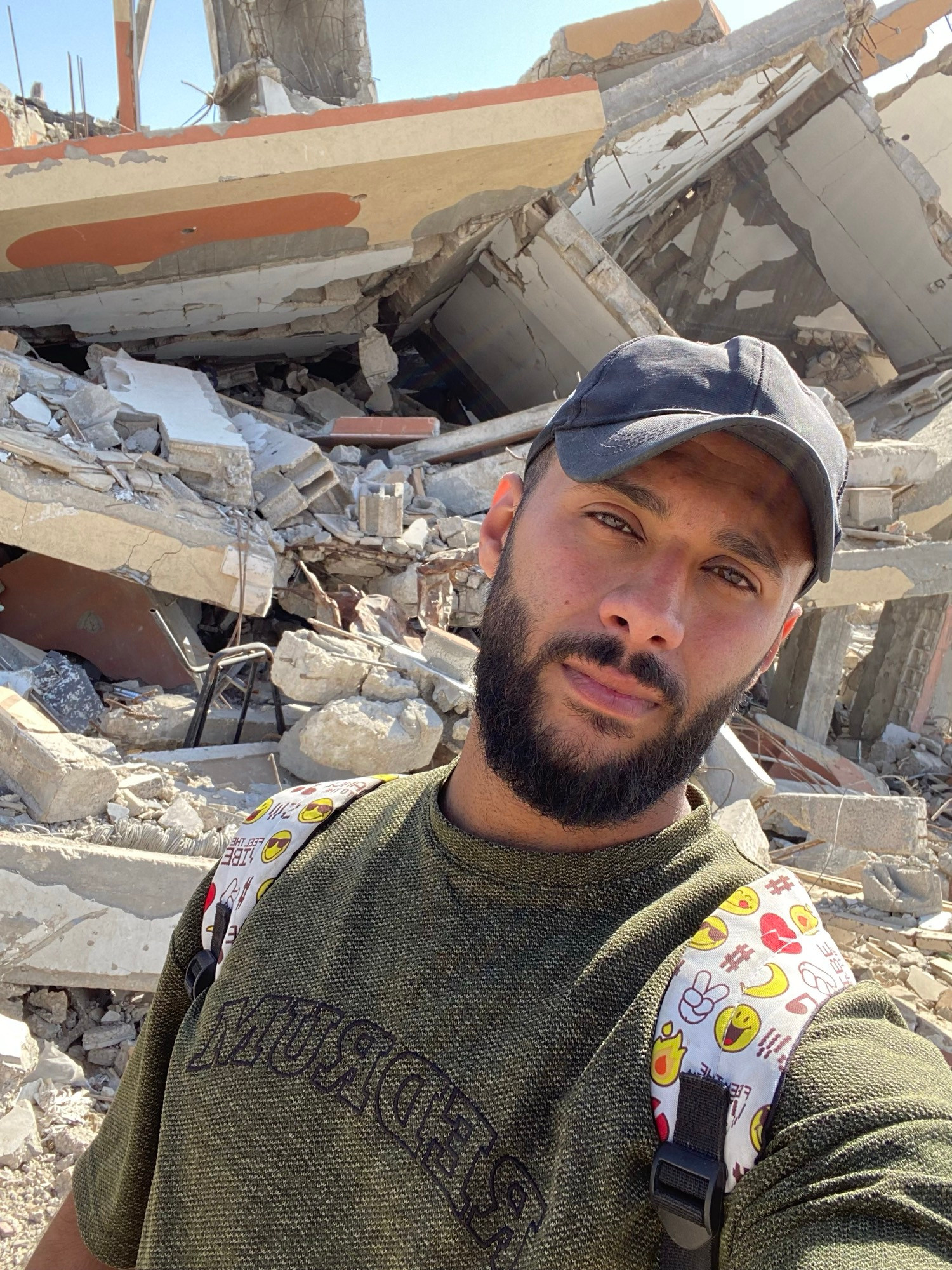 A Palestinian young man from Gaza stands with a pale, exhausted face against a backdrop of destruction. His eyes speak of hunger, waiting, and fading hope.