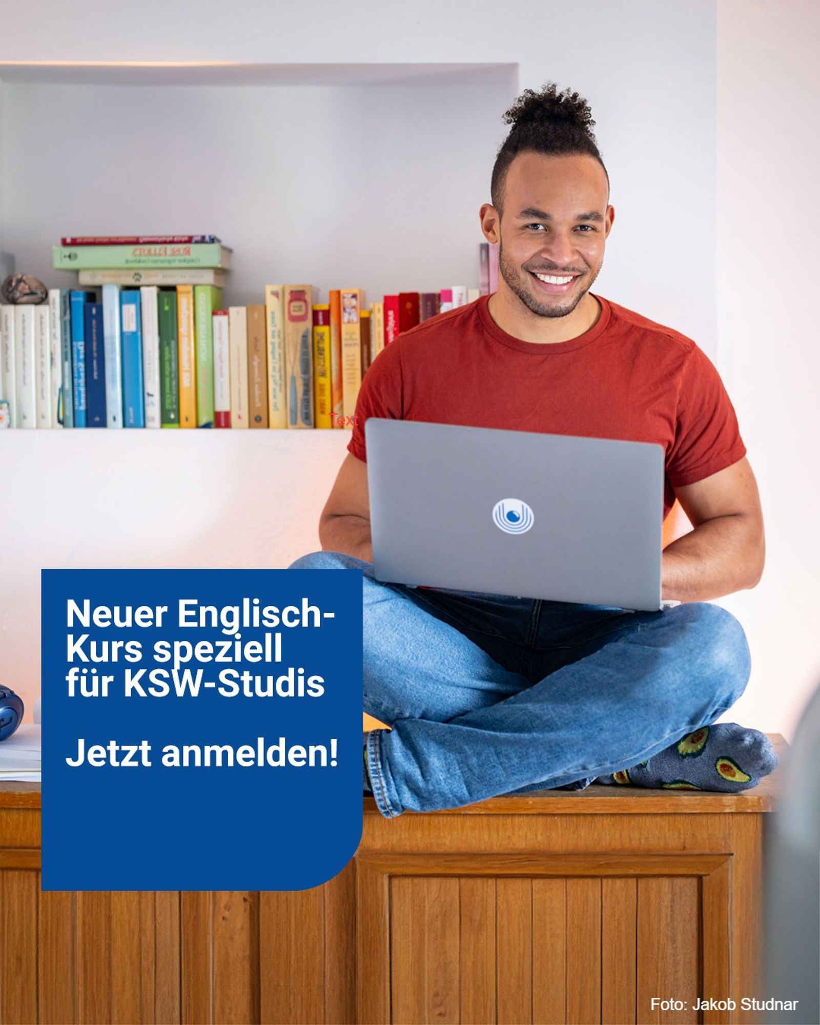 ein Mann sitzt mit gekreuzten Beinen auf einem Bett und einem Laptop.