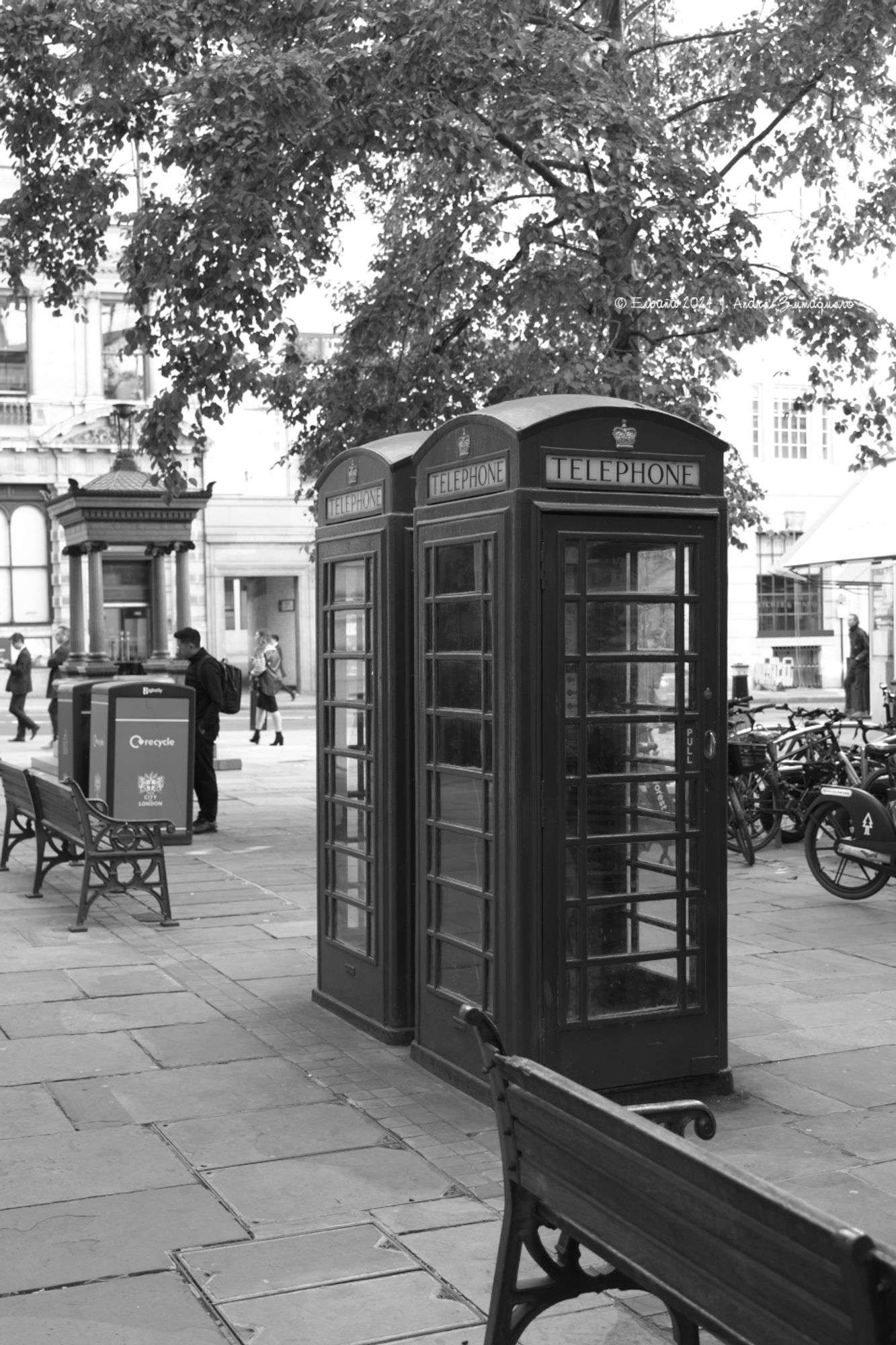 Dos típicas cabinas telefónicas londinenses juntas en una acera de la ciudad. La fotografía es en blanco y negro.