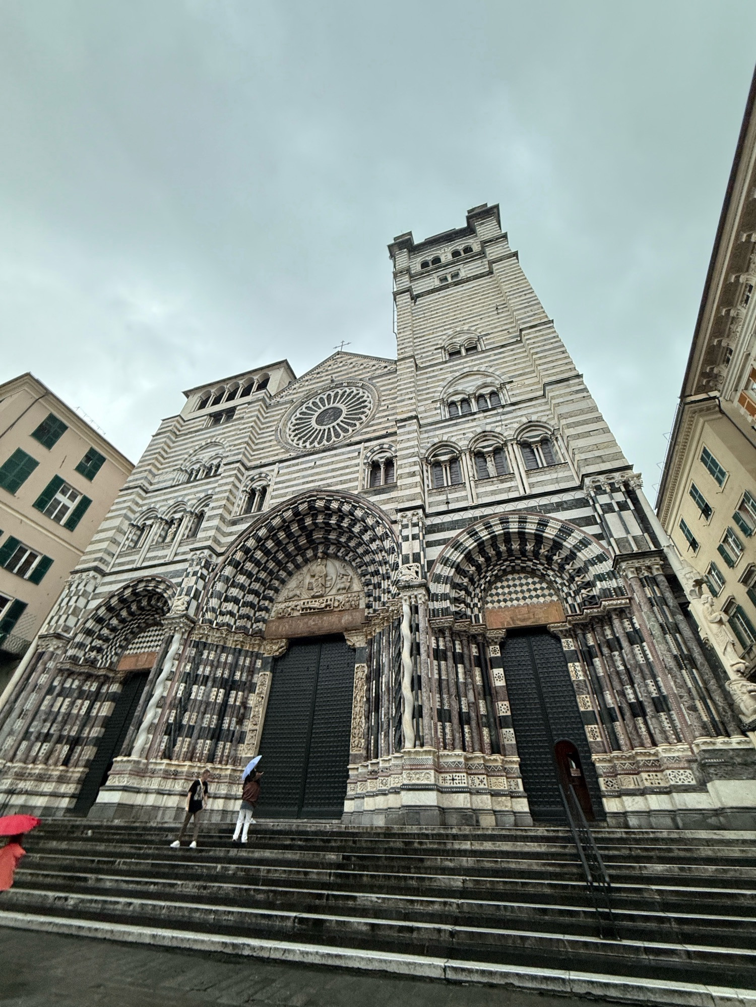 The front of San Lorenzo Cathedral, a white and grey striped stone building. The weather is lousy.