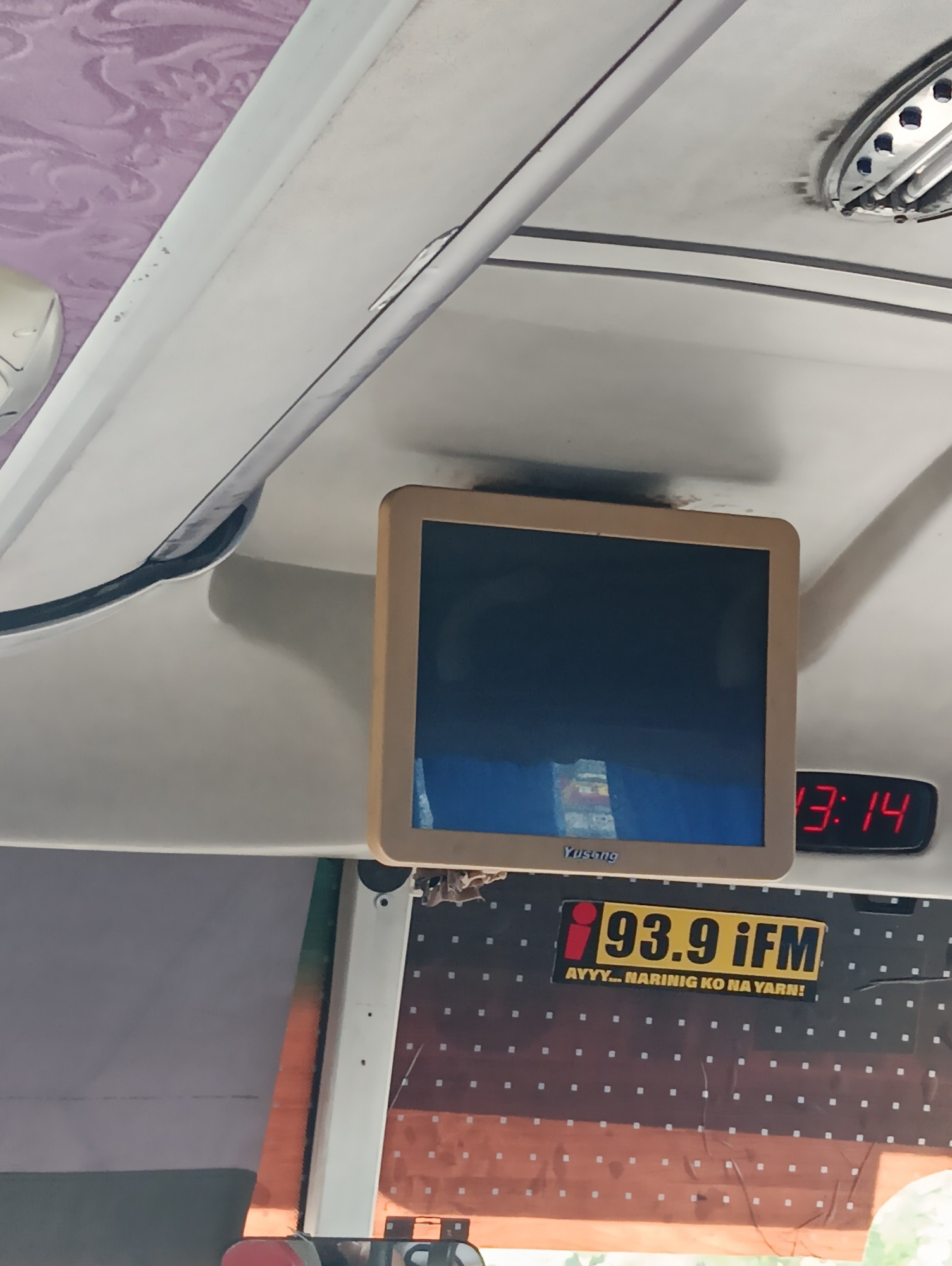 a random photo of a bus ceiling with the digital clock visible showing 13:14