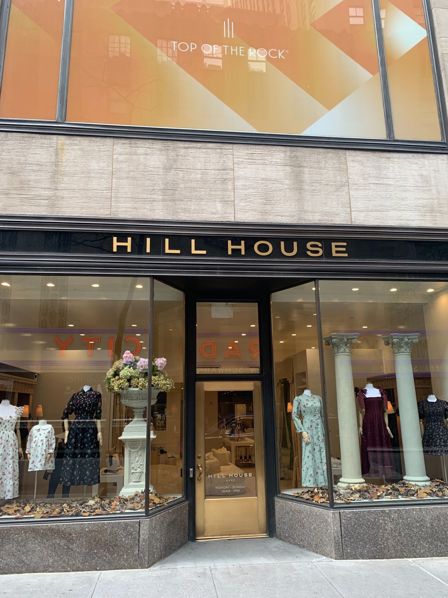 A women's clothing store in Rockefeller Center called HILL HOUSE, displaying dresses (with the RADIO CITY MUSIC HALL sign reflected backwards in the window).